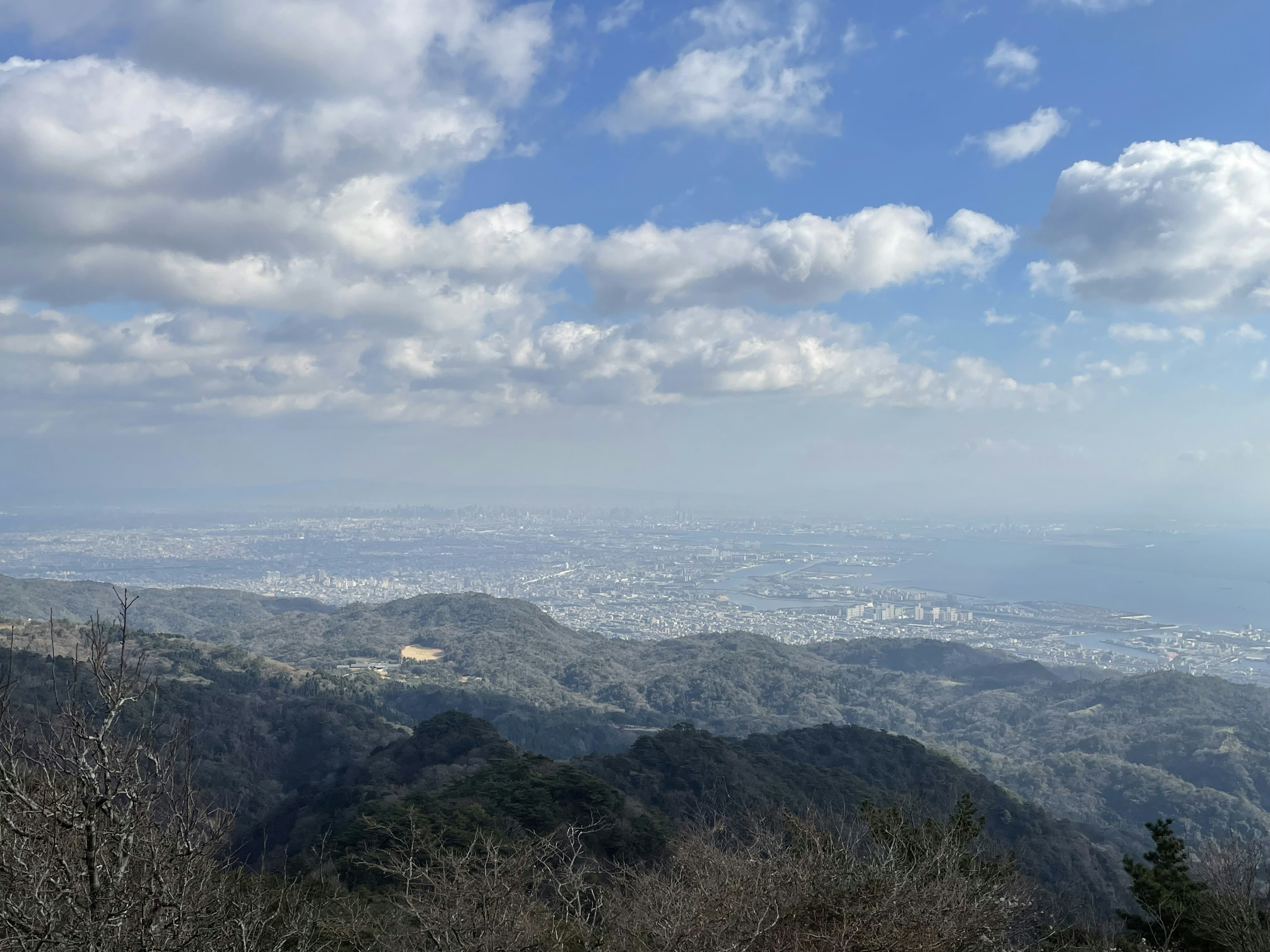 Paisaje montañoso con cielo azul y nubes árboles verdes en primer plano vista de la ciudad lejana