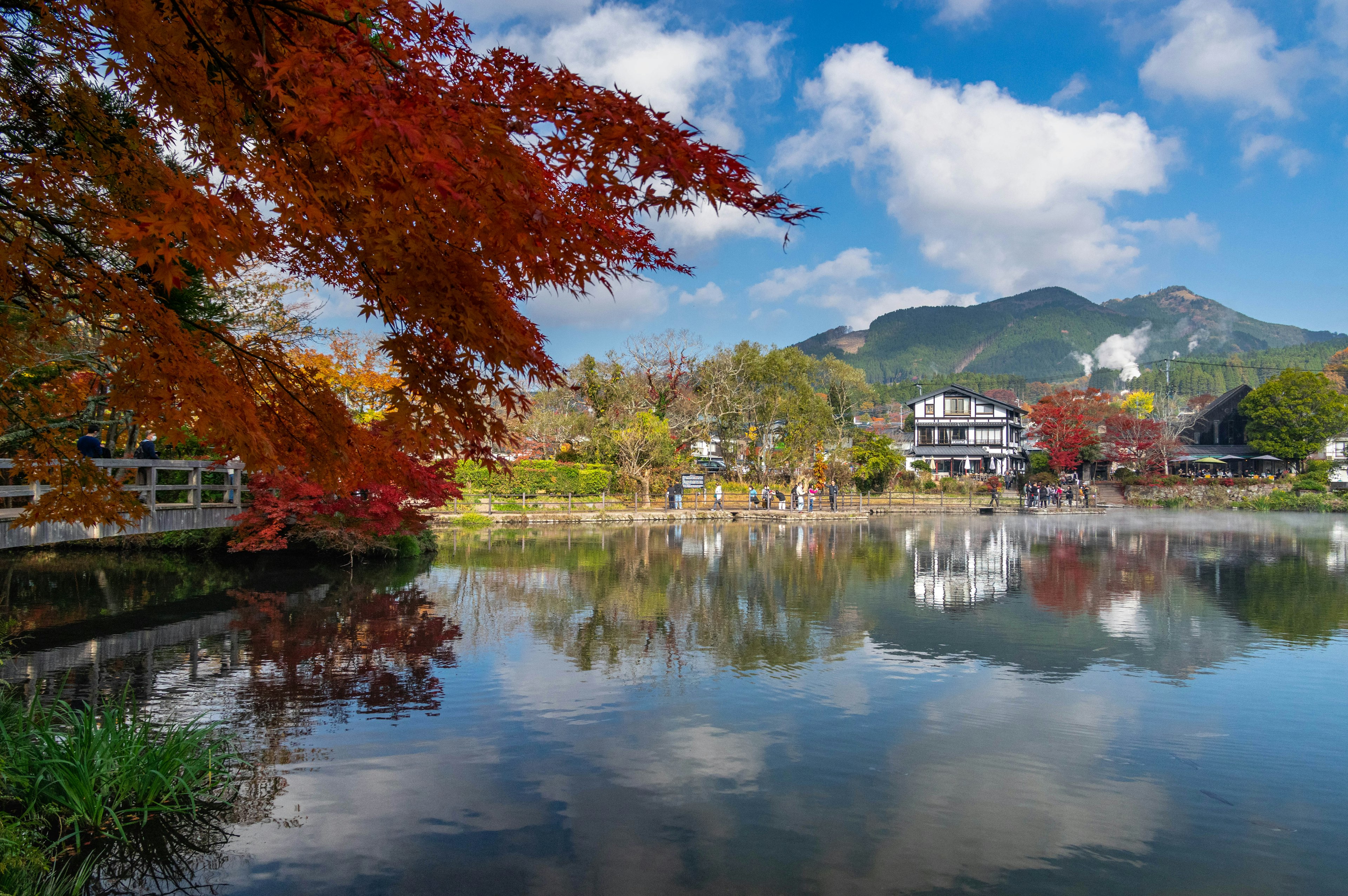 秋季风景，五彩斑斓的树叶在宁静的湖面上倒影，周围是山脉和蓝天