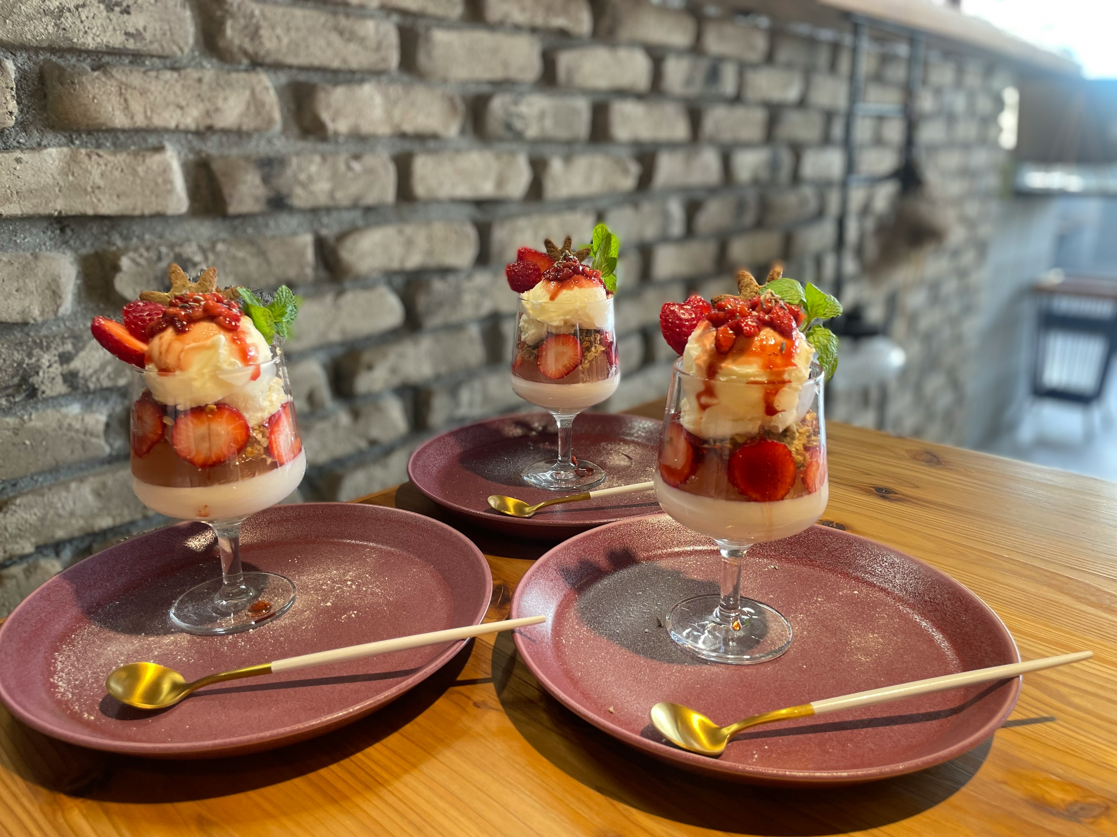 Tres copas de postre llenas de parfait de fresas y plátanos sobre una mesa de madera