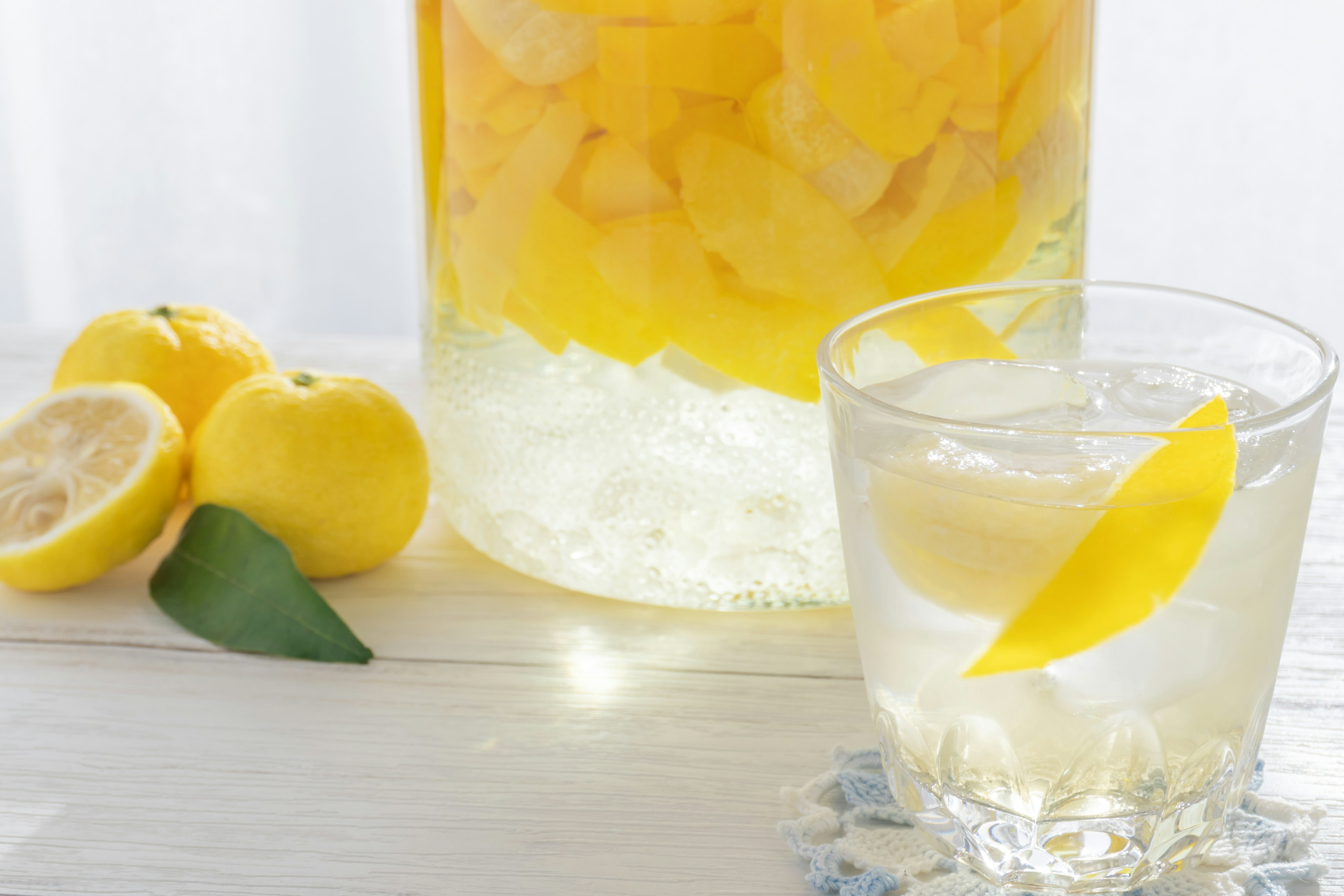 Un verre de boisson claire avec des glaçons et des tranches de citron à côté de citrons entiers