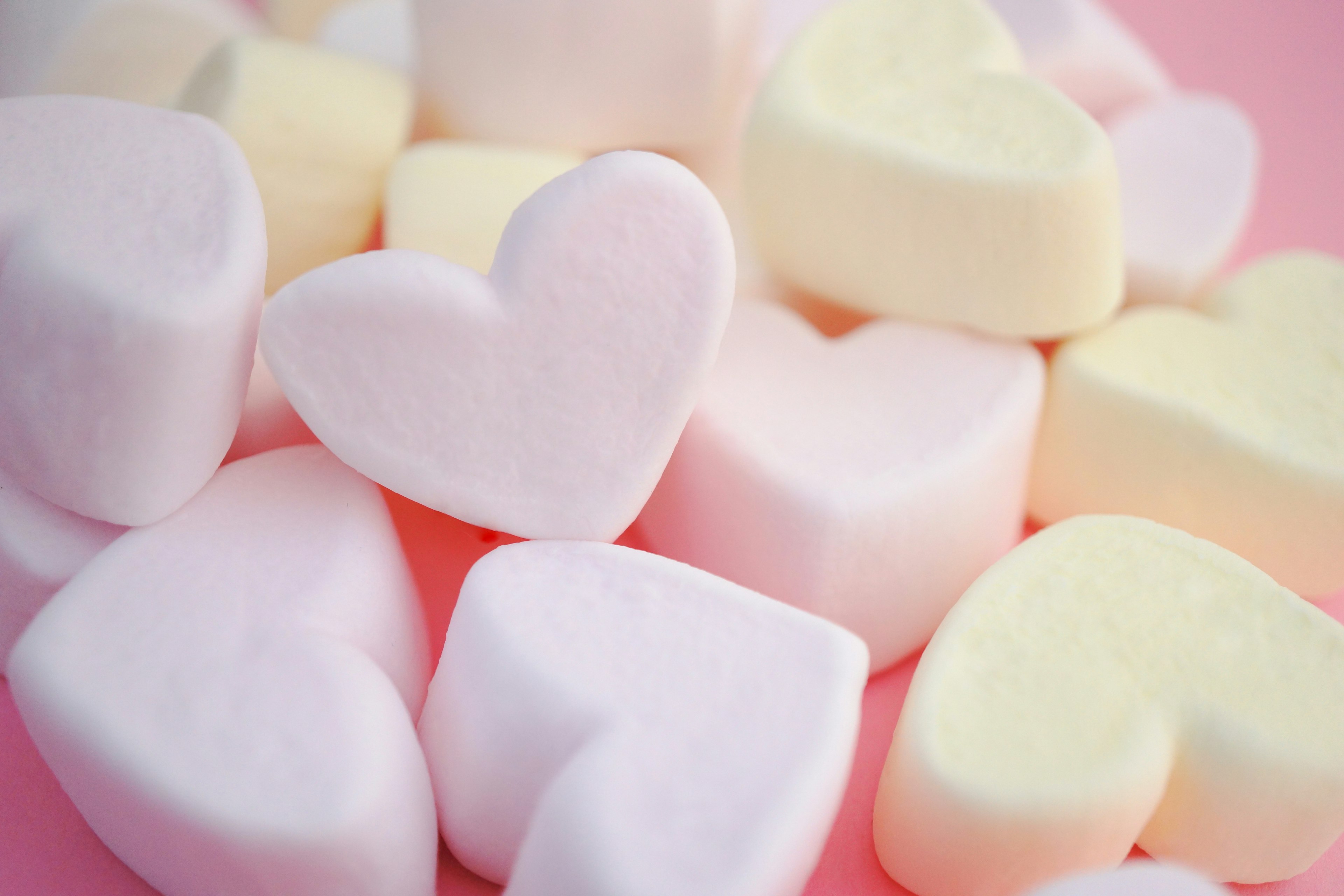 Heart-shaped marshmallows scattered on a pink background