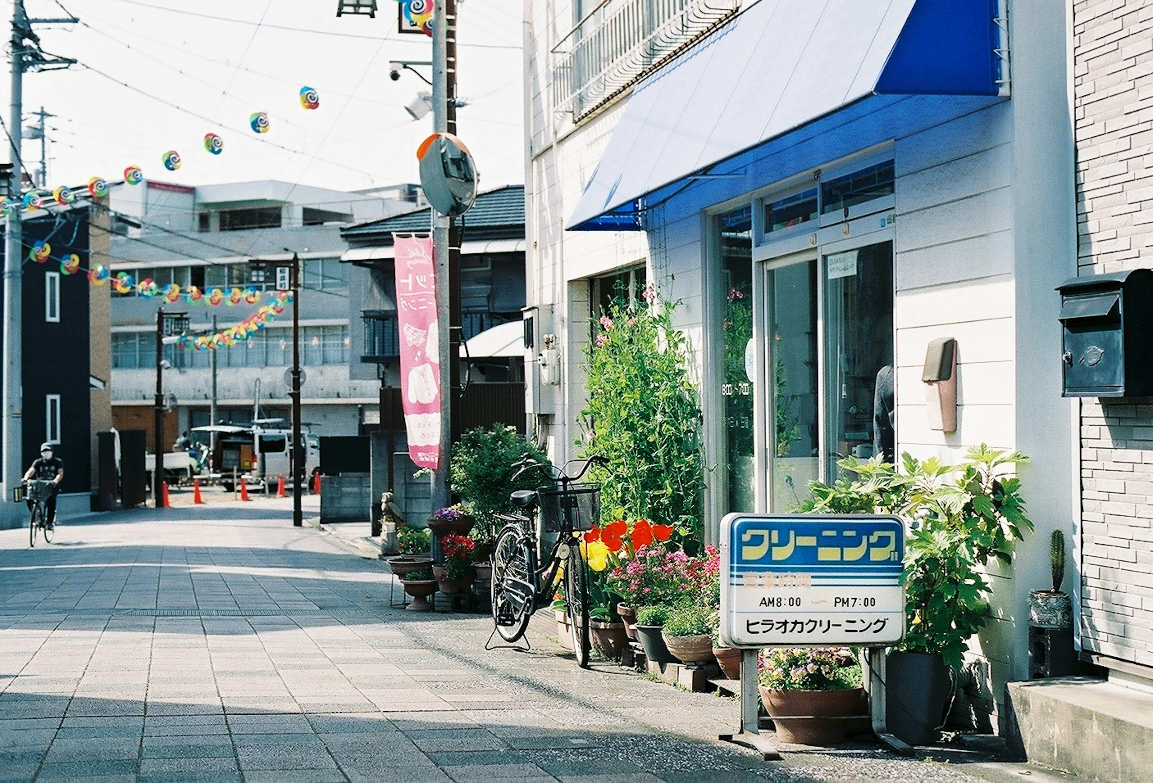 青い屋根の店舗と花が飾られた歩道の風景