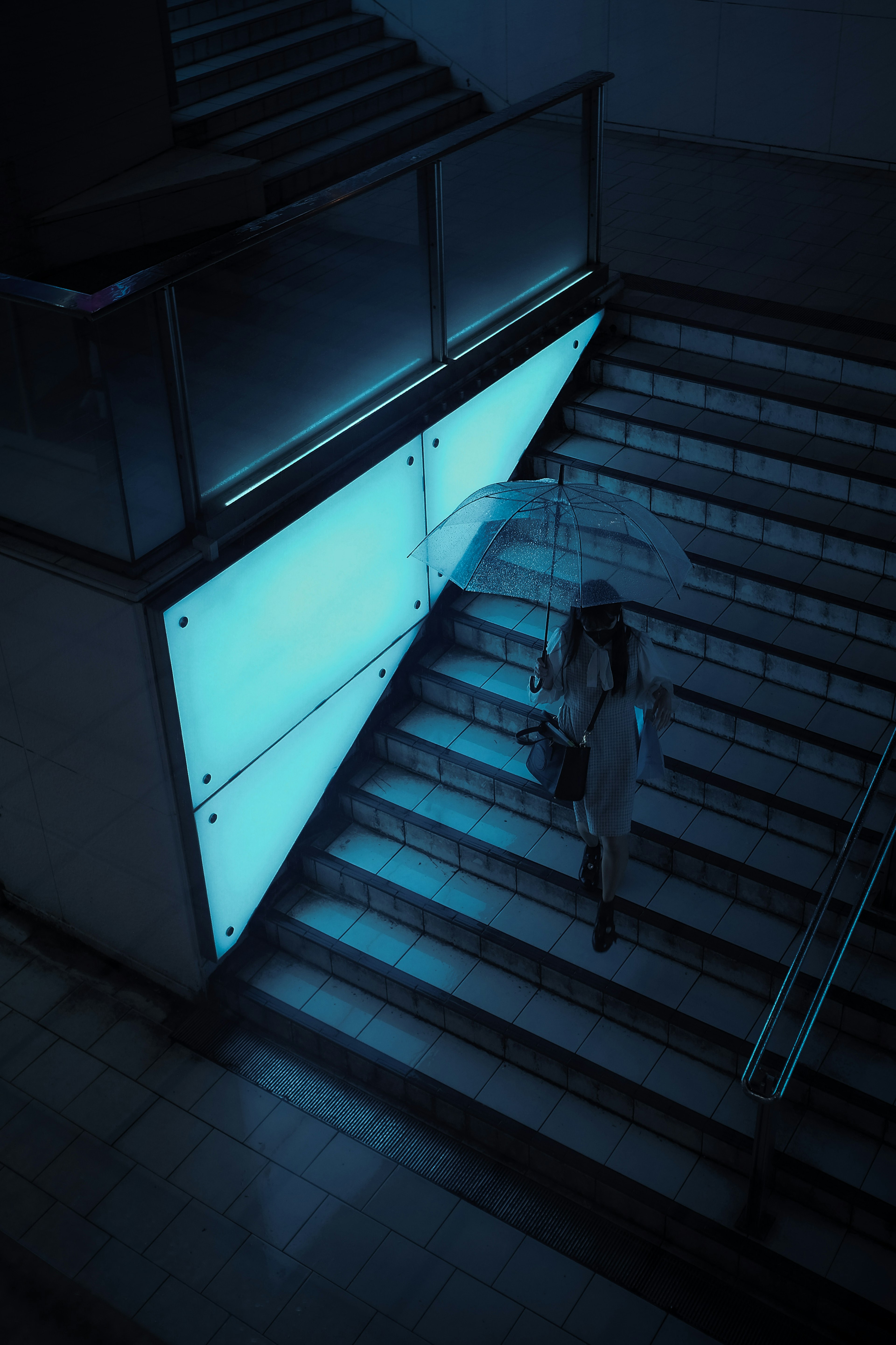 Una mujer con un paraguas bajando escaleras iluminadas por luz azul