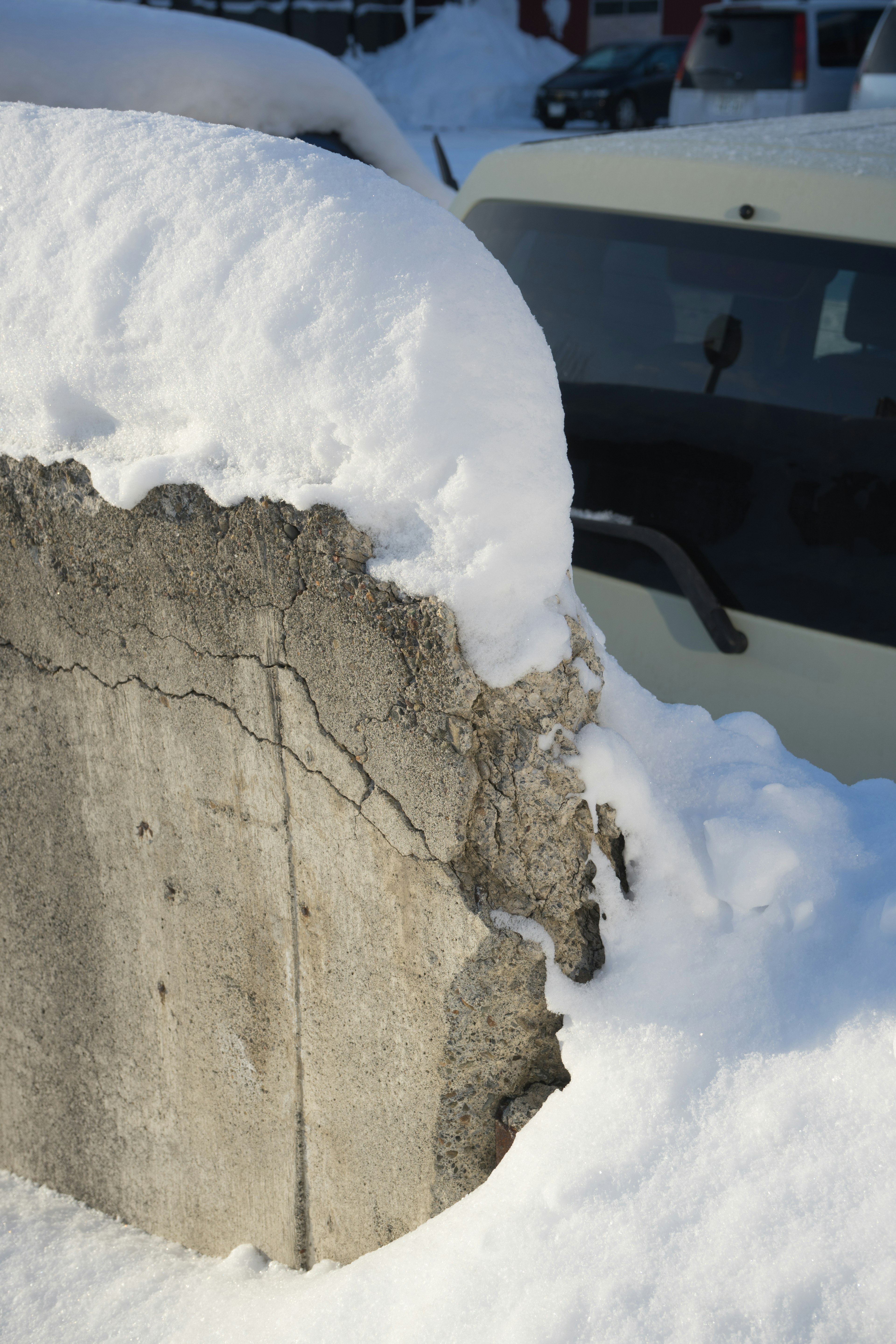 Teil einer mit Schnee bedeckten Betonwand mit einem Auto dahinter