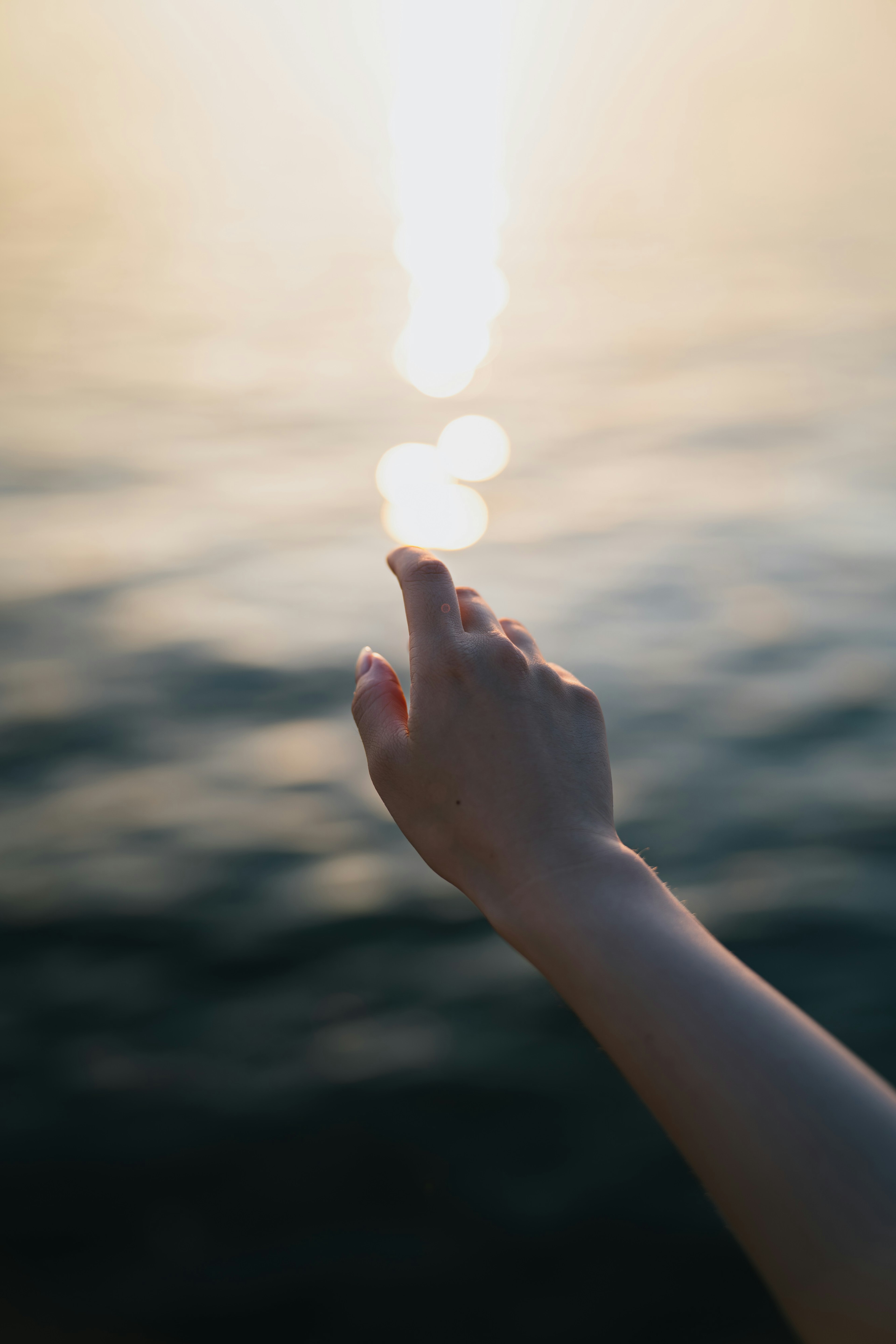 Silhouette di una mano che si estende verso la superficie dell'acqua e luce brillante