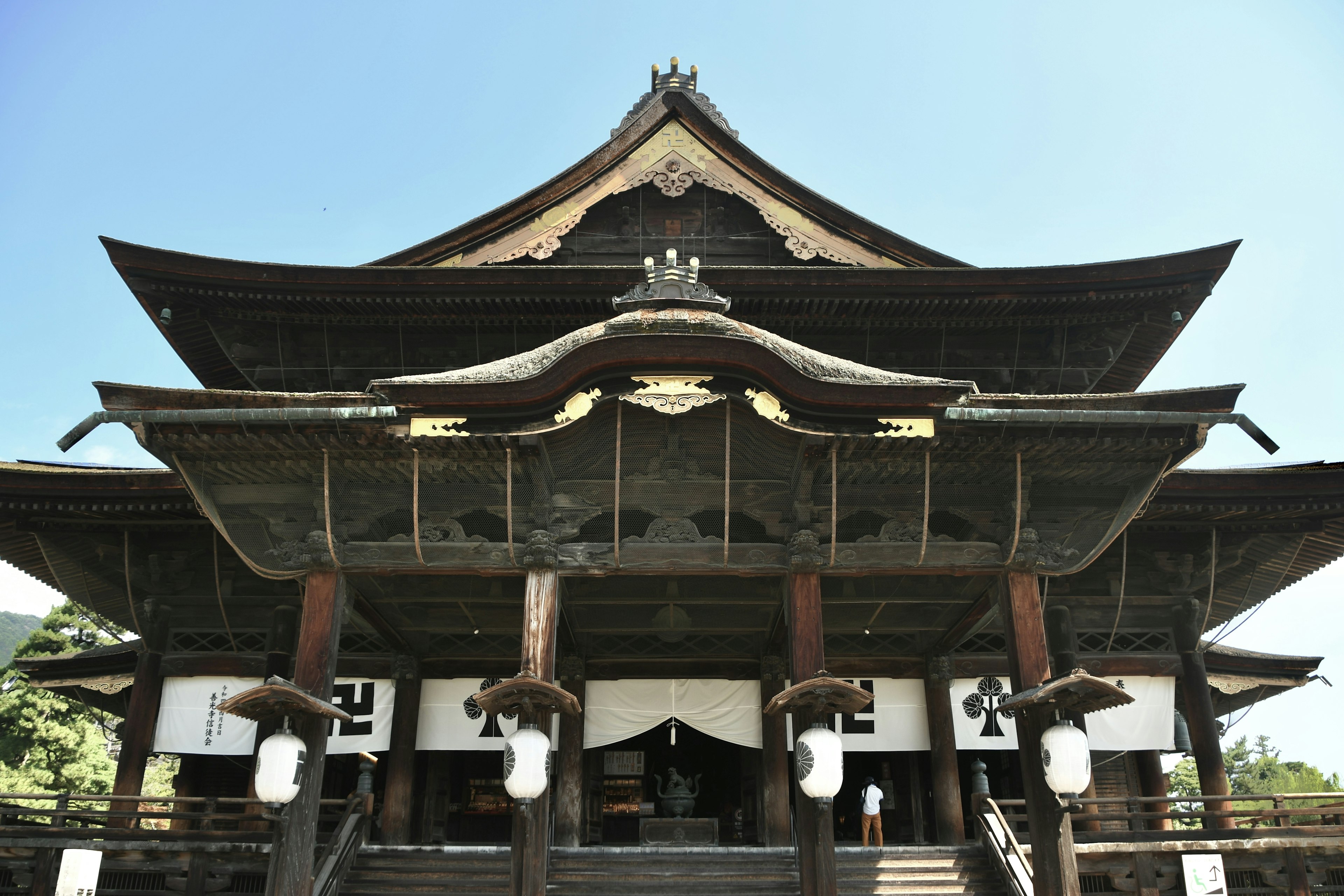 Photo of the front entrance of a large wooden temple featuring a curved and decorative roof