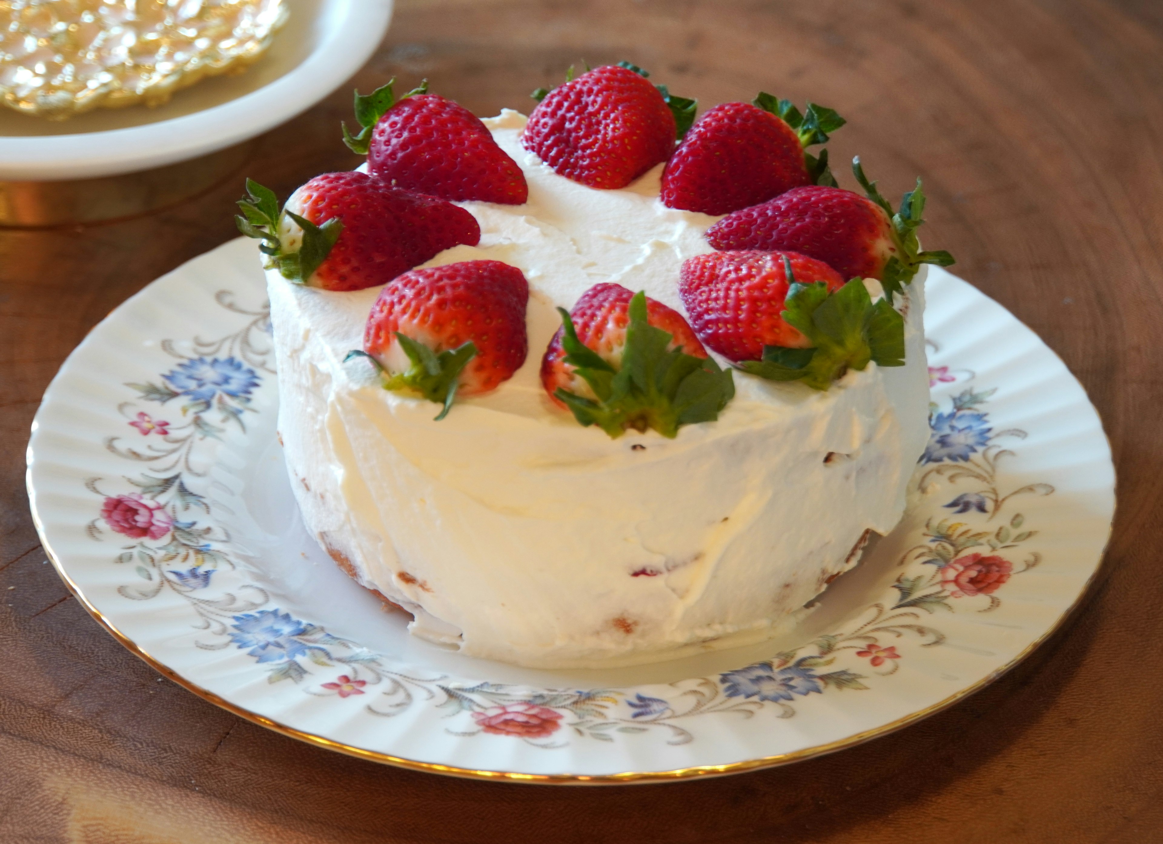 A cream cake topped with strawberries on a floral plate