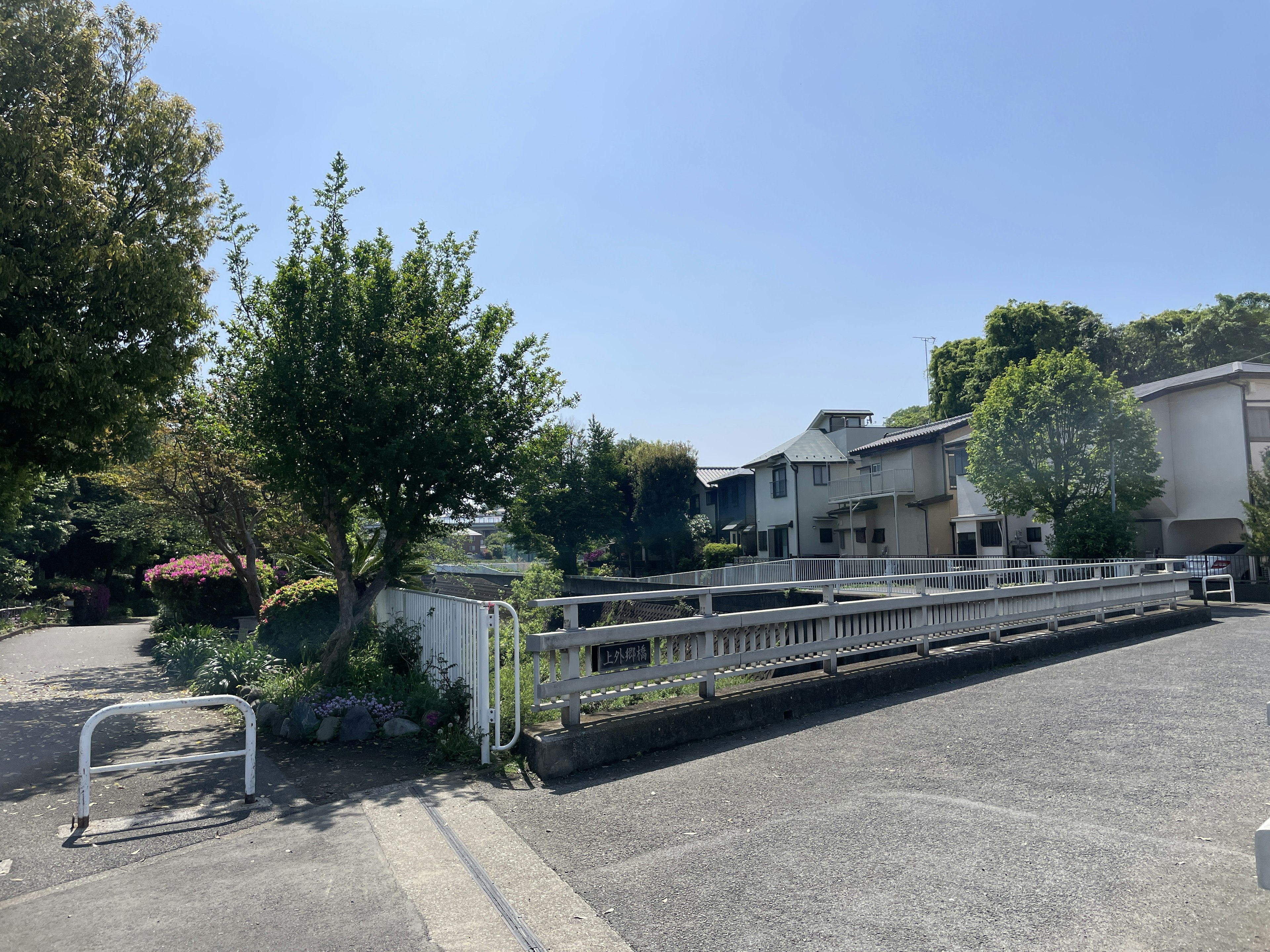 Residential area scene under blue sky featuring green trees and white fence