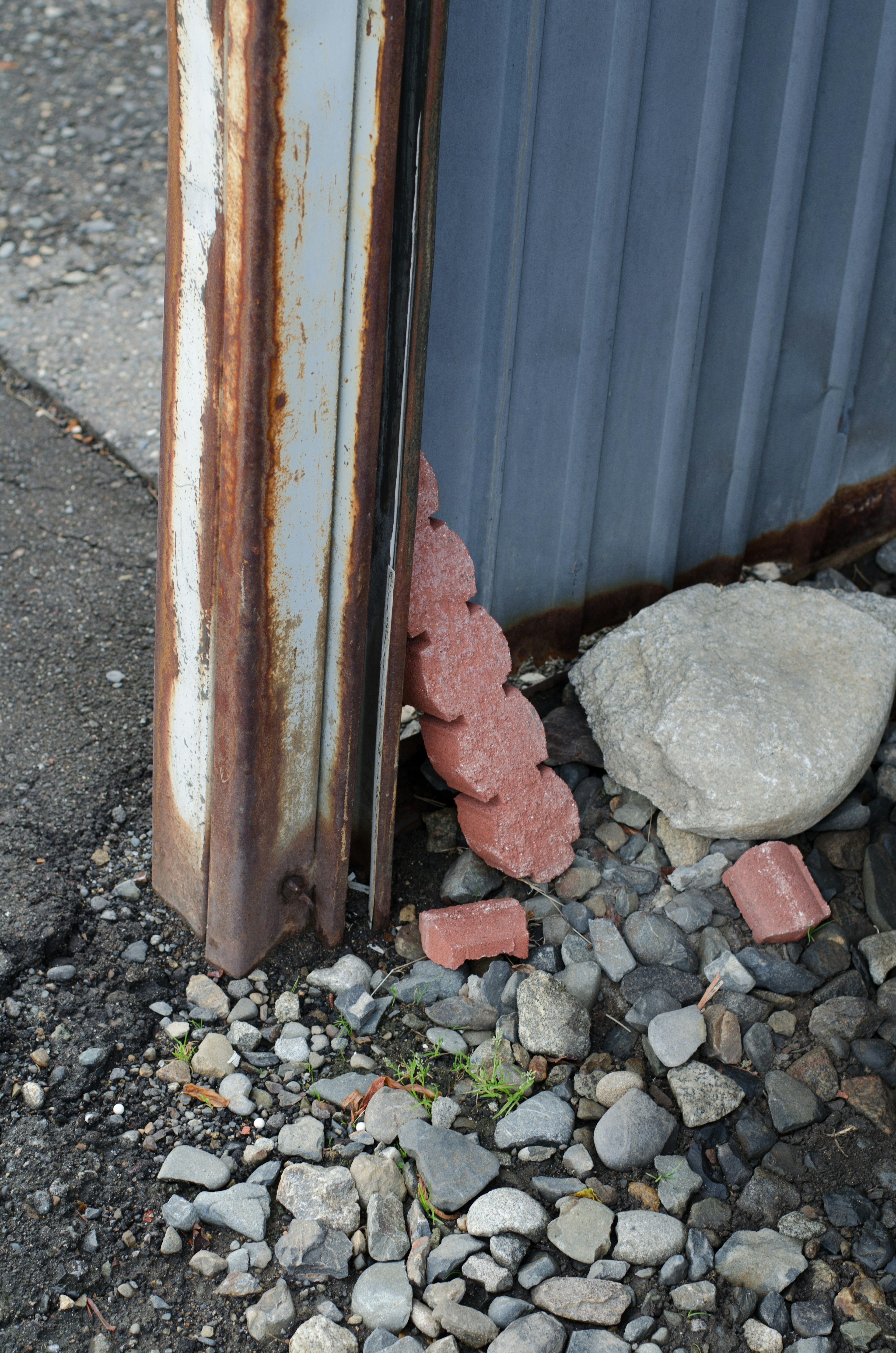 A row of bricks stacked between a rusty metal post and a gray wall