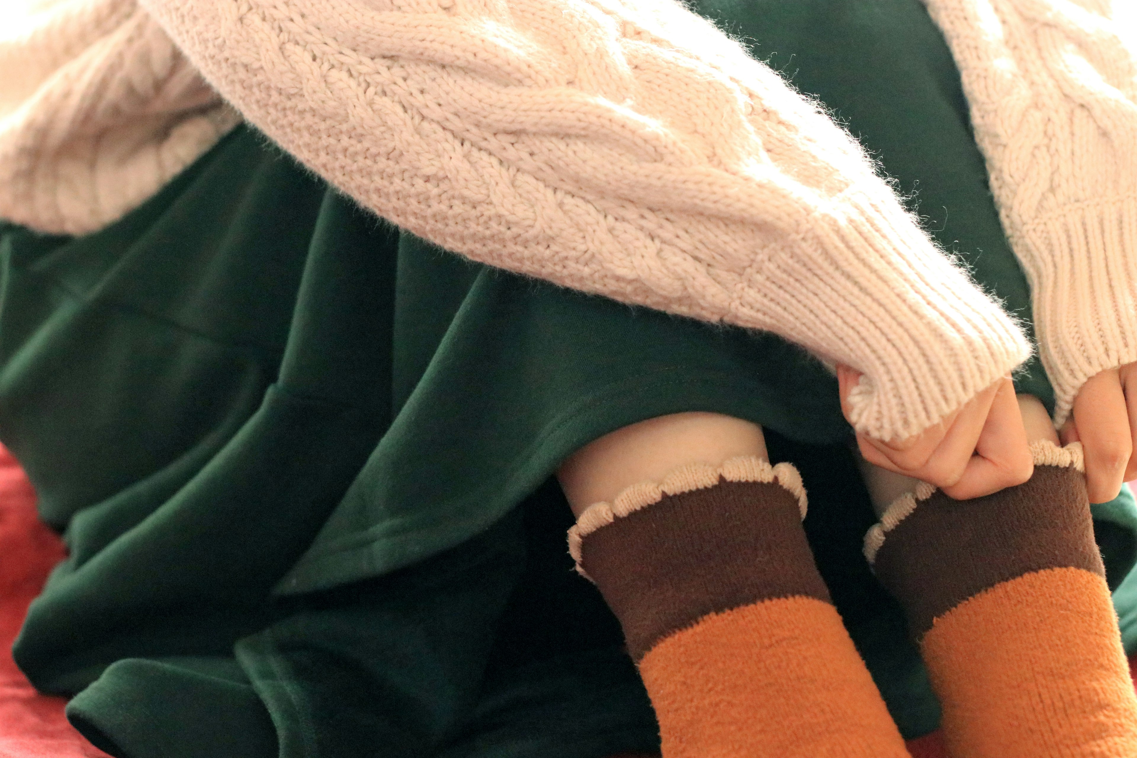 A woman wearing a green skirt and a white sweater is sitting. She has orange and brown socks