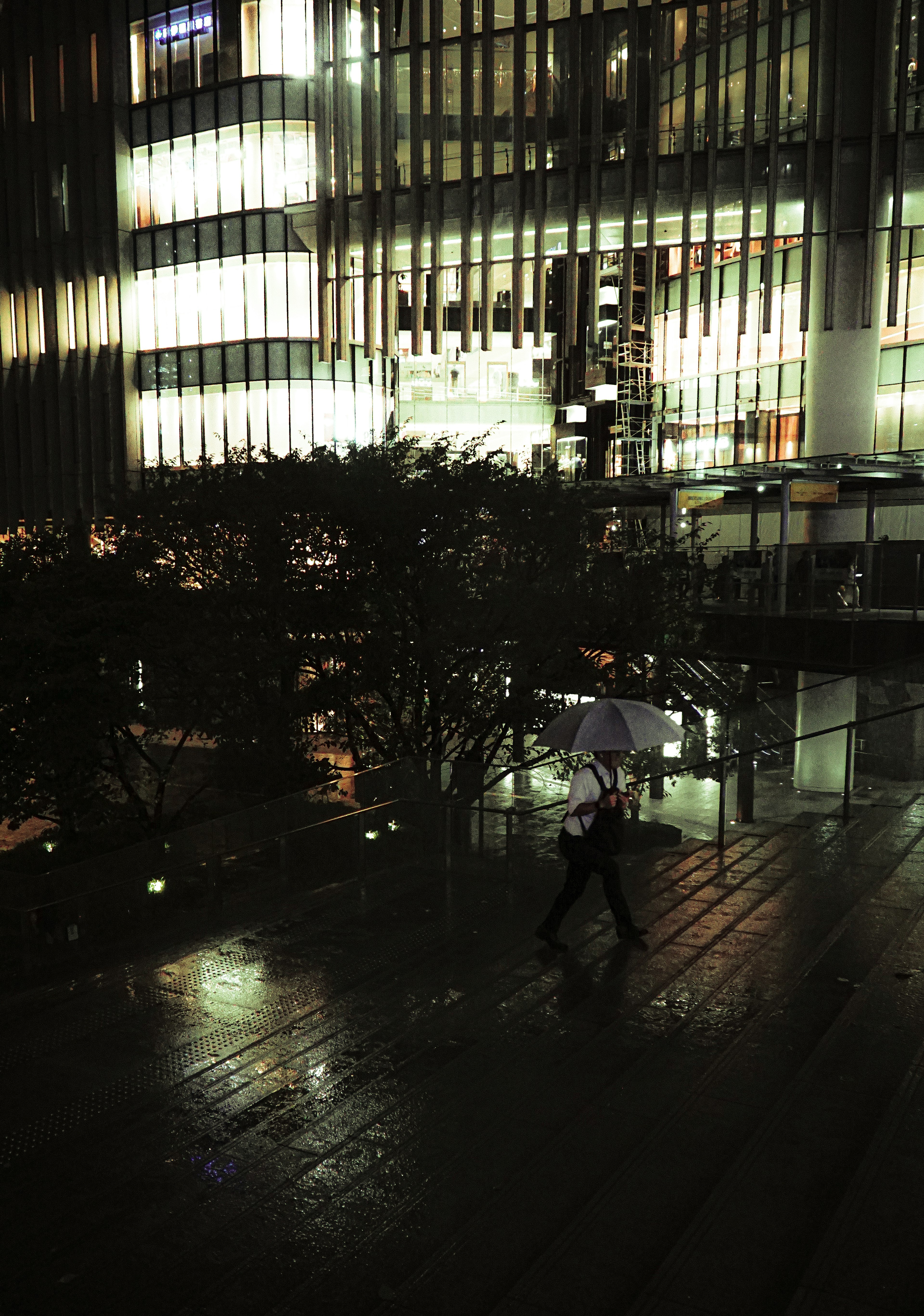 Una persona caminando con un paraguas bajo la lluvia cerca de un edificio moderno por la noche