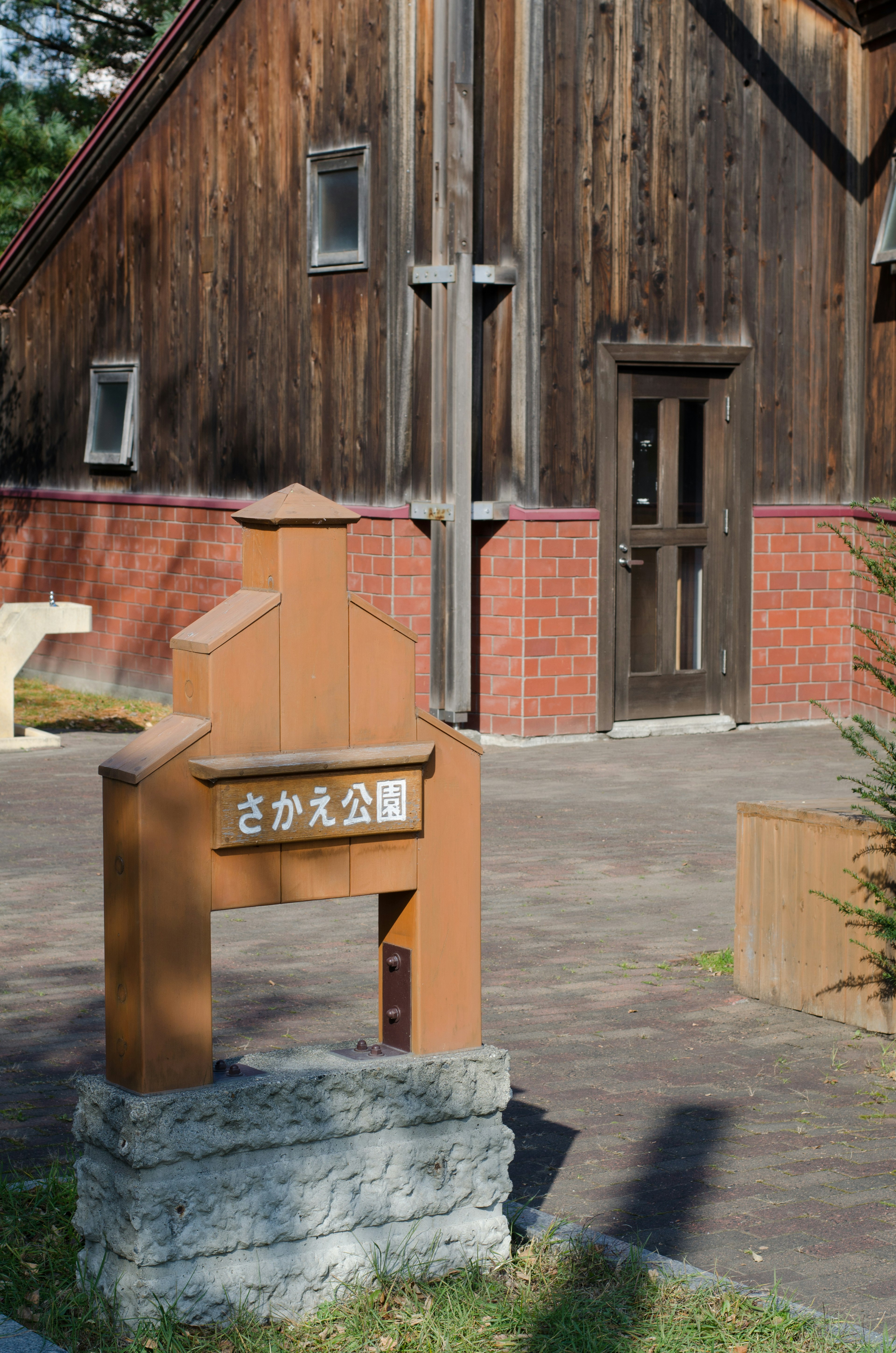 Parkeingang mit Holzschild und rotem Backsteingebäude