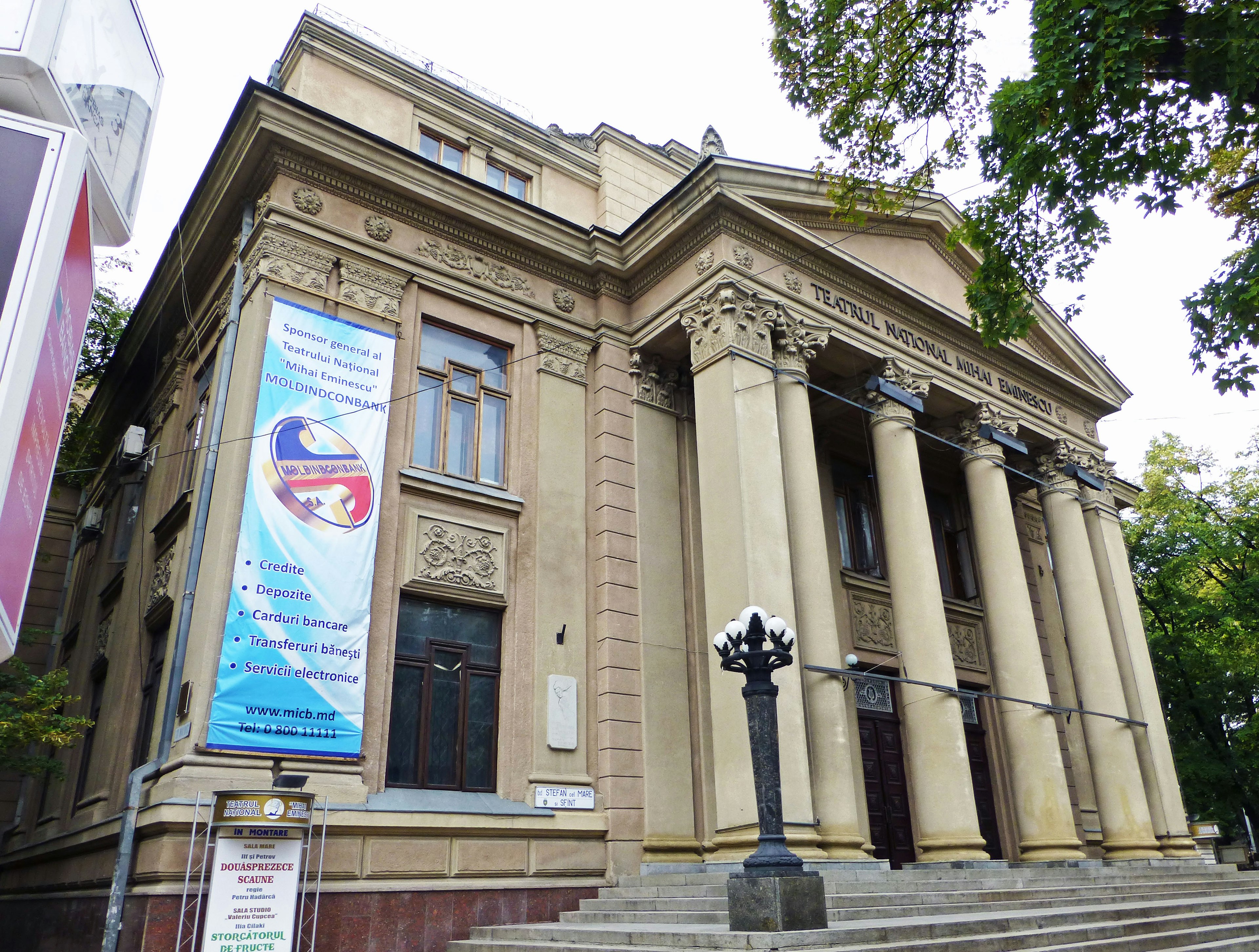 Exterior de un edificio histórico con grandes columnas y detalles ornamentales con una farola y un letrero