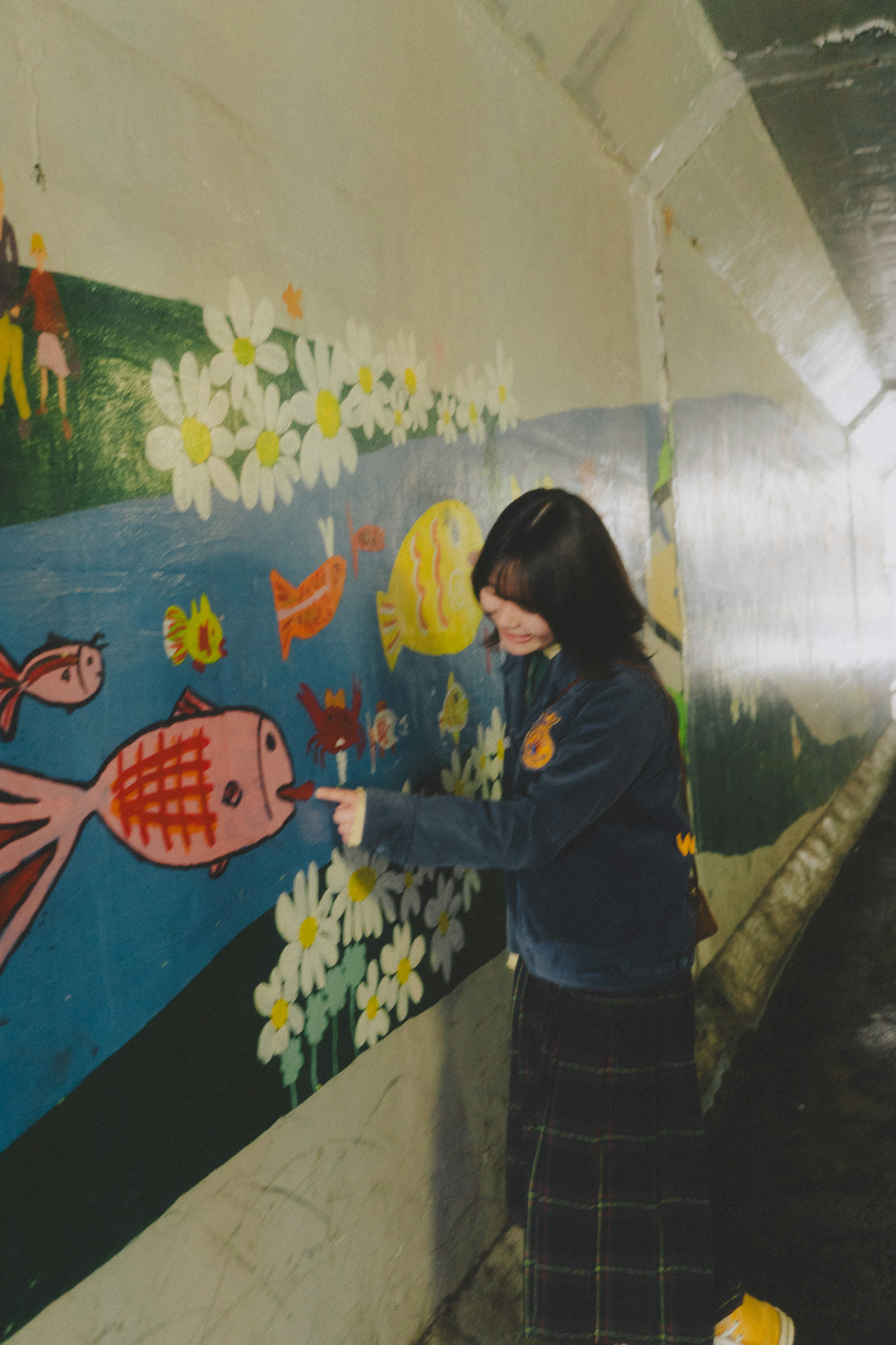 Chica interactuando con un mural que presenta peces coloridos y flores en un túnel brillante