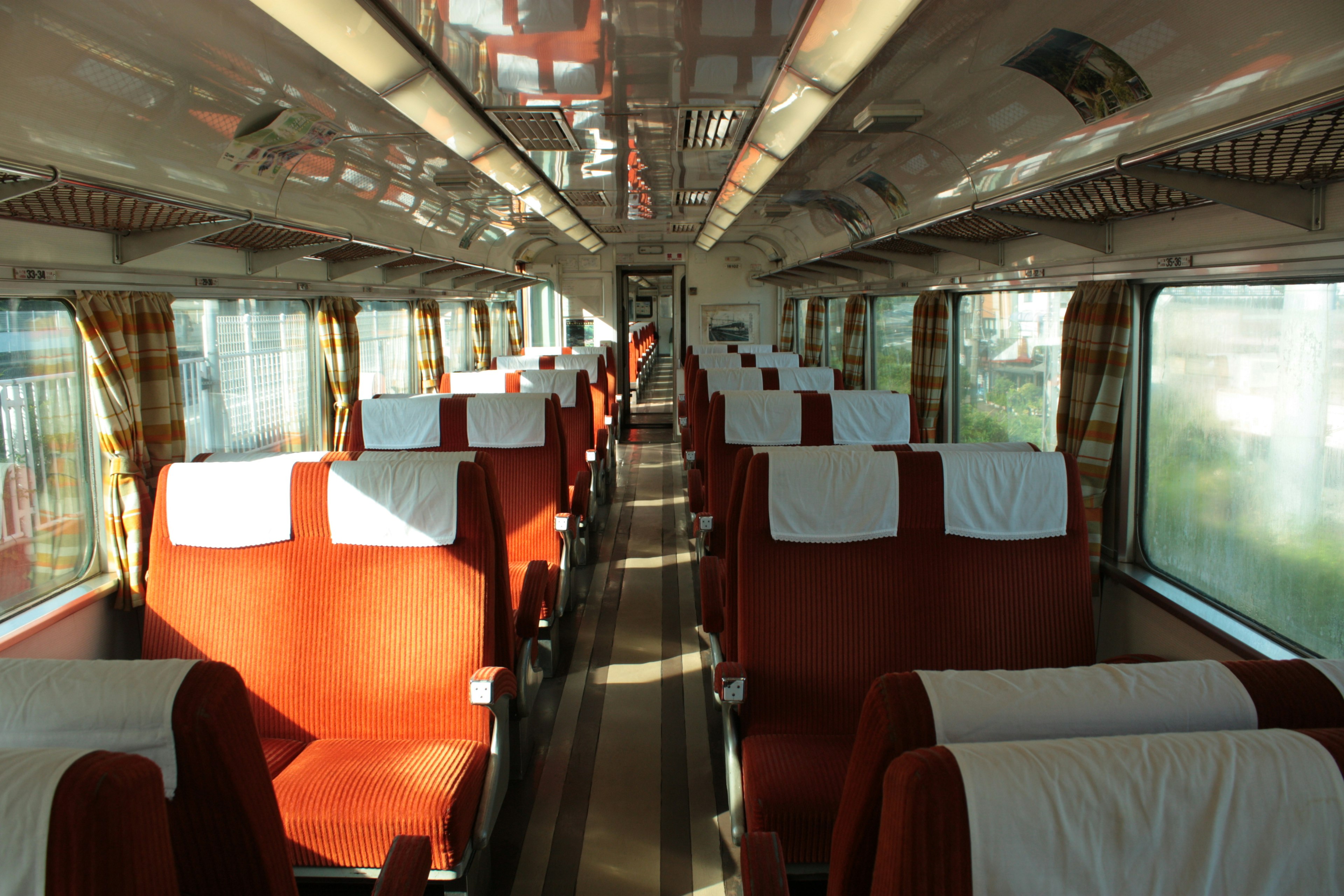 Interno di un carrozza di treno luminoso con sedili rossi ordinati e luce naturale dalle finestre