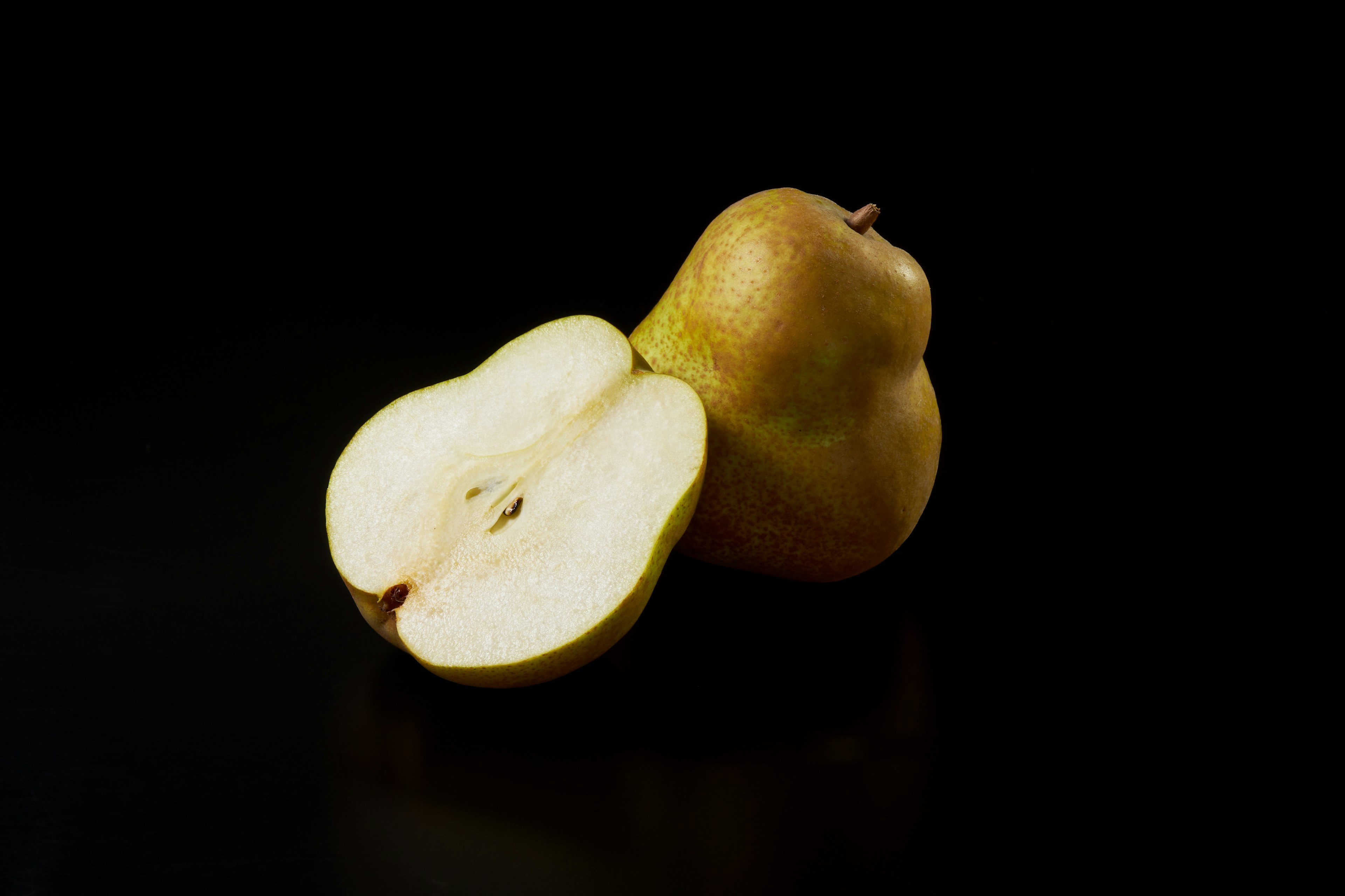 A whole pear and a halved pear on a black background