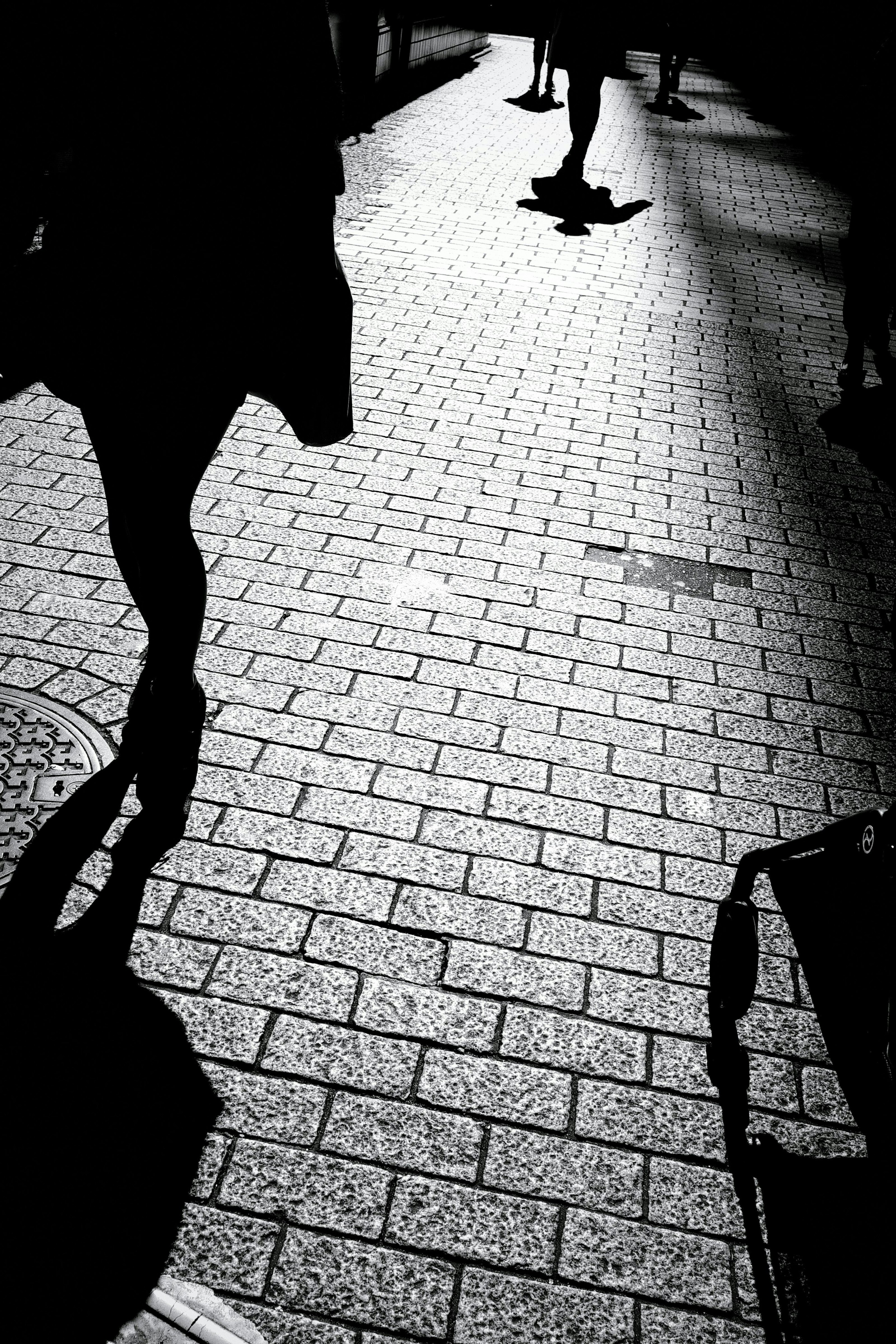 Silhouettes of people walking on tiled pavement in shadows