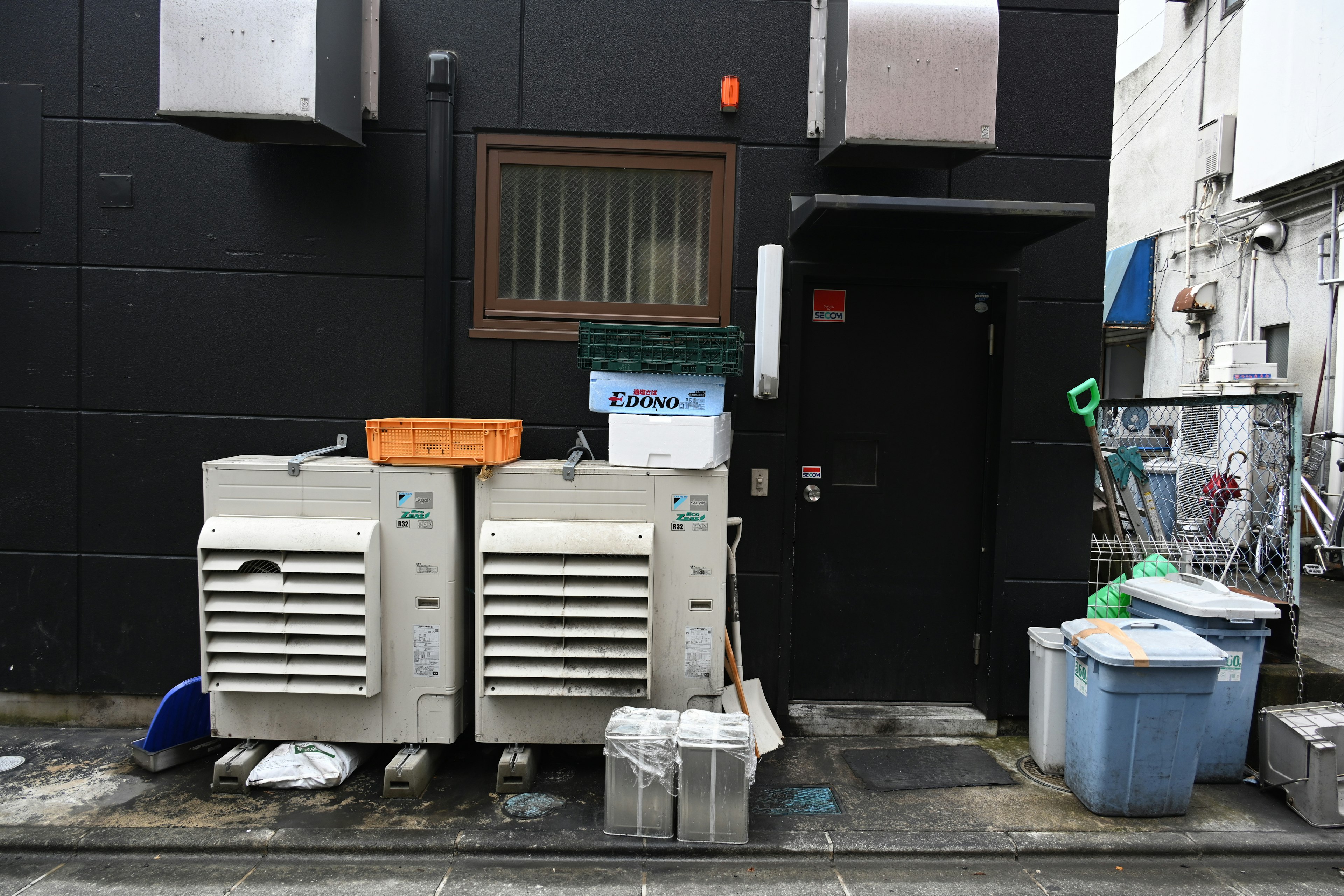 Puerta trasera con unidades de refrigeración y cubos de basura contra una pared negra