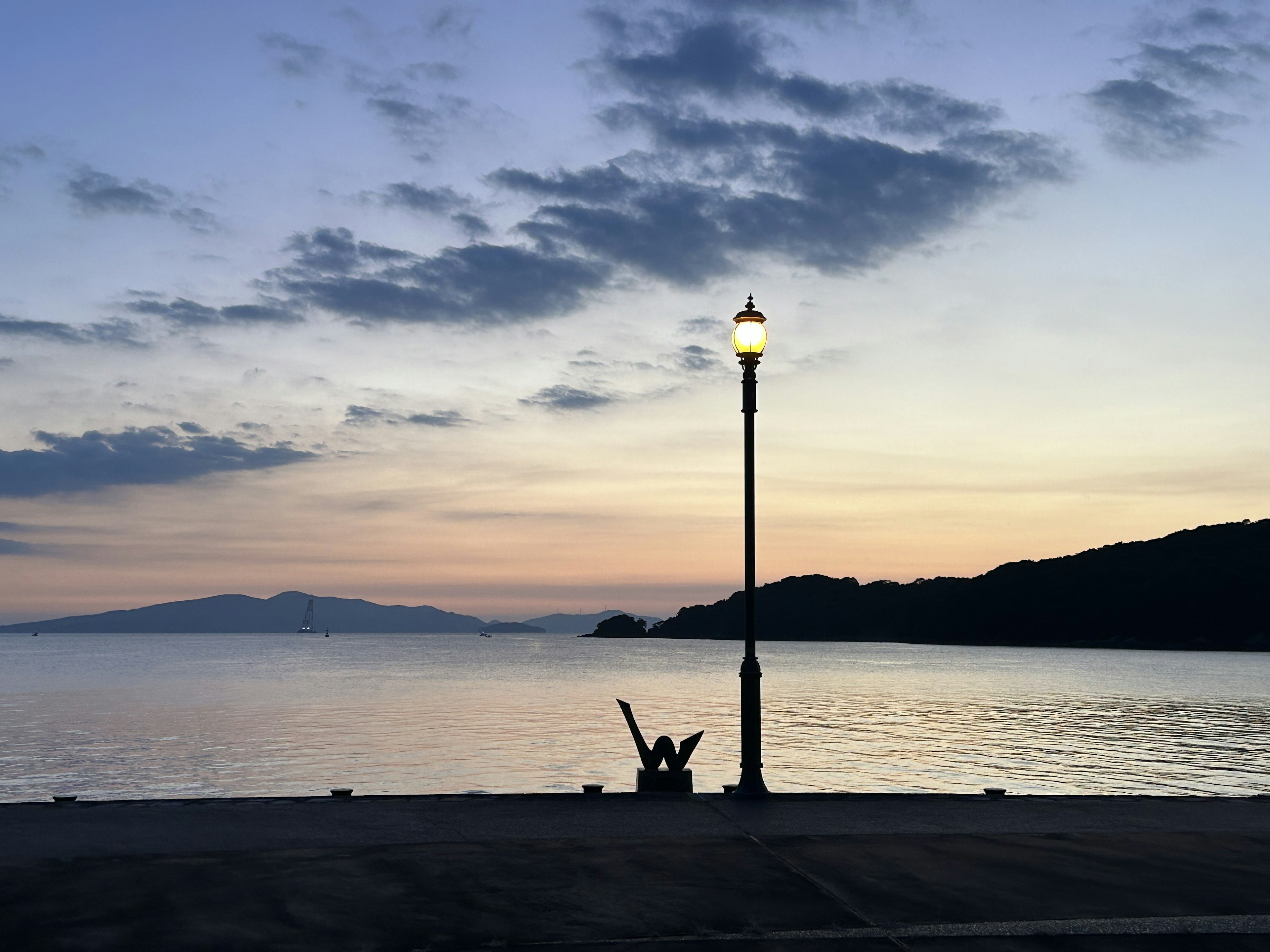 夕暮れ時の海岸で、街灯の前に座る人影が見える