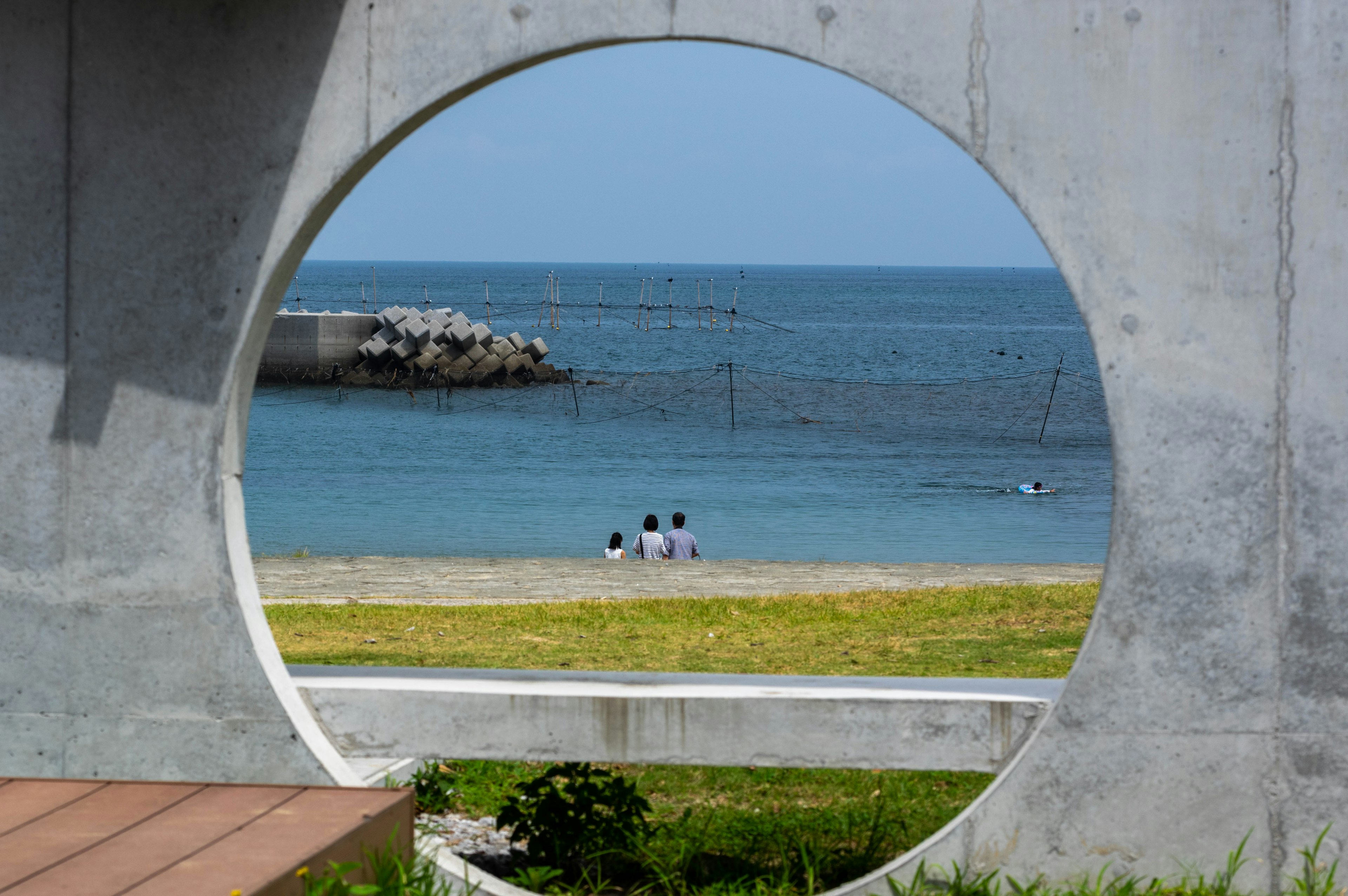 丸いコンクリートの枠越しに見える海と砂浜で座っている人々