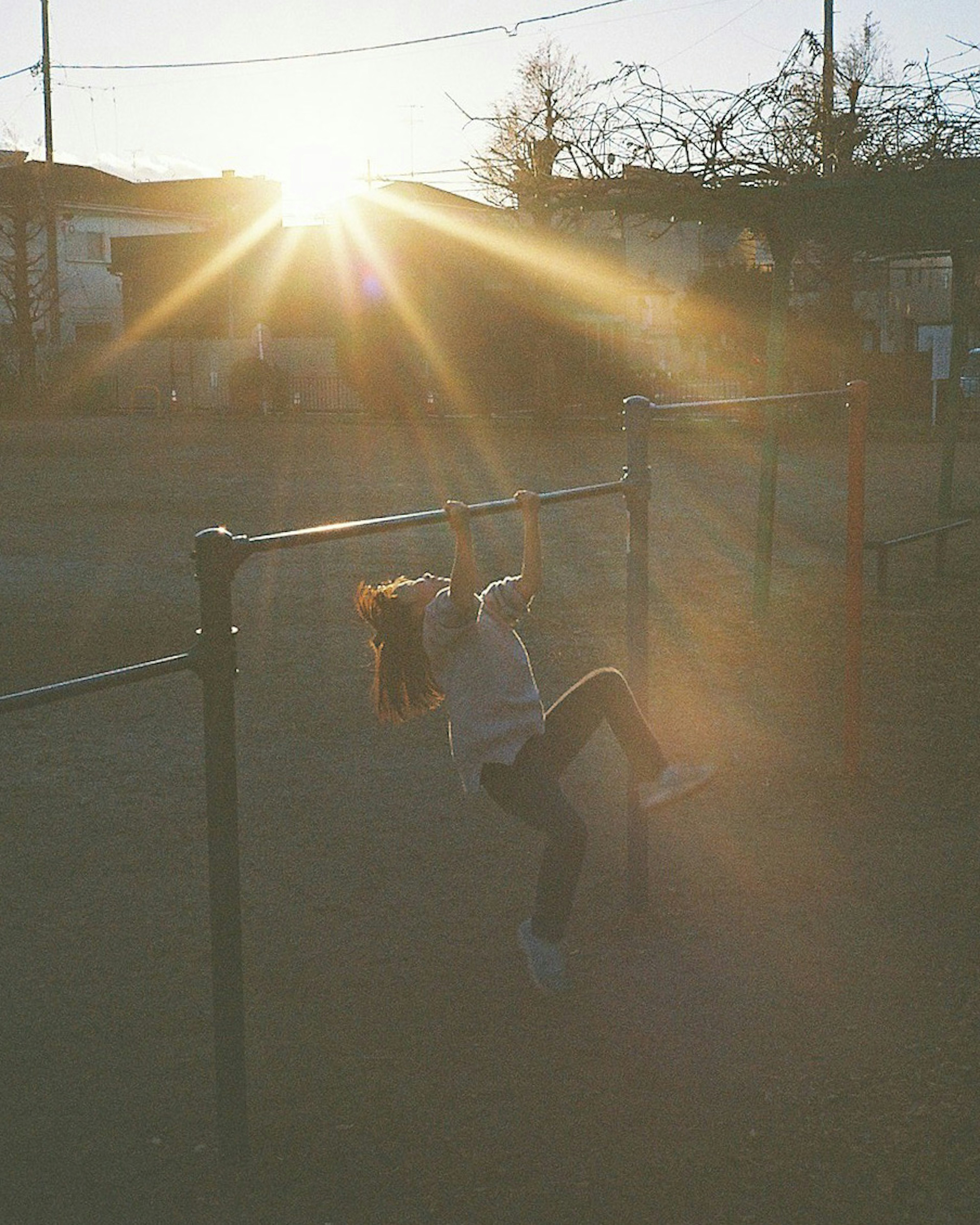 Child playing on playground equipment with a glowing sunset in the background