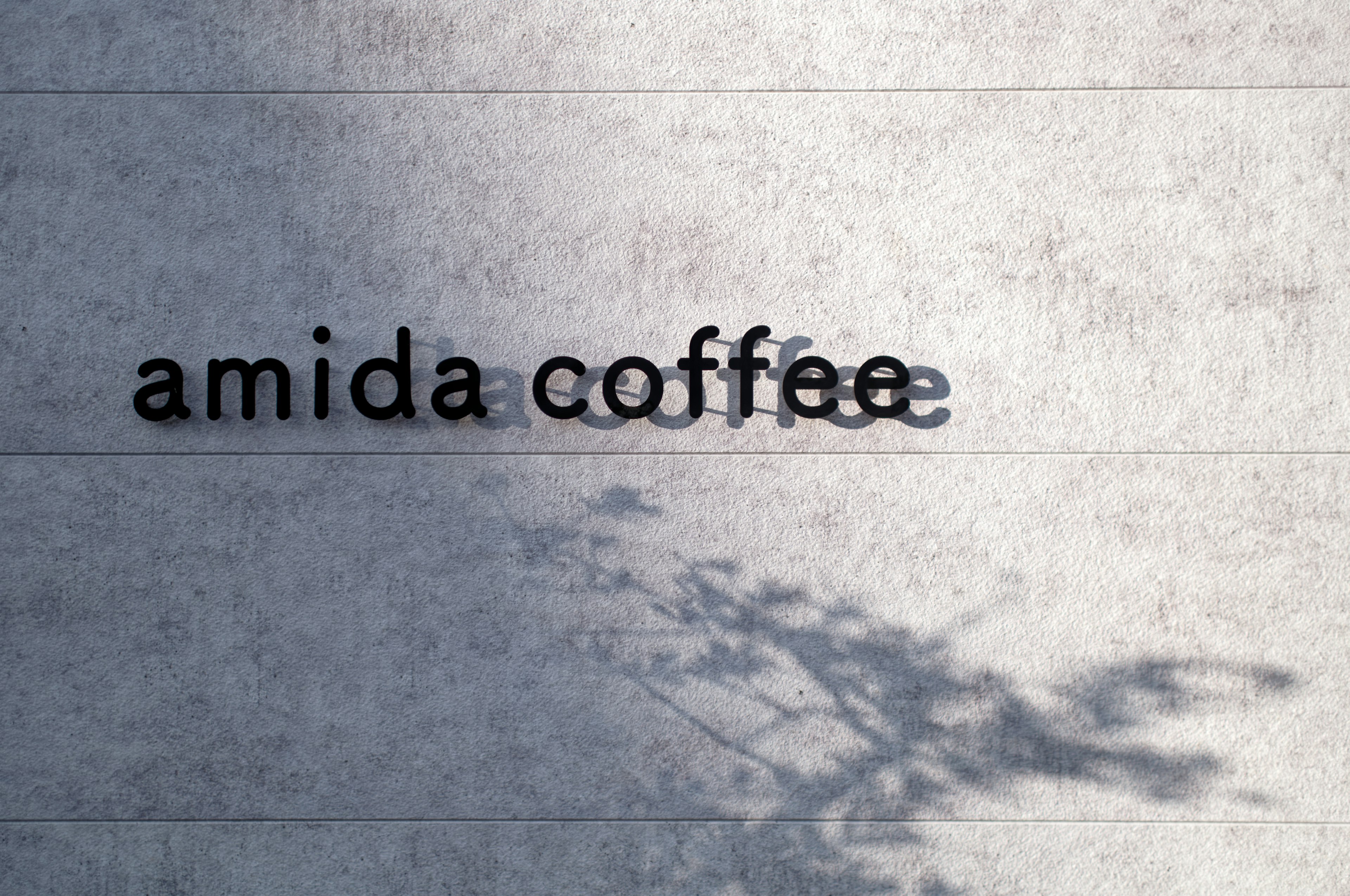 Amida Coffee logo displayed on a concrete wall with shadow effects