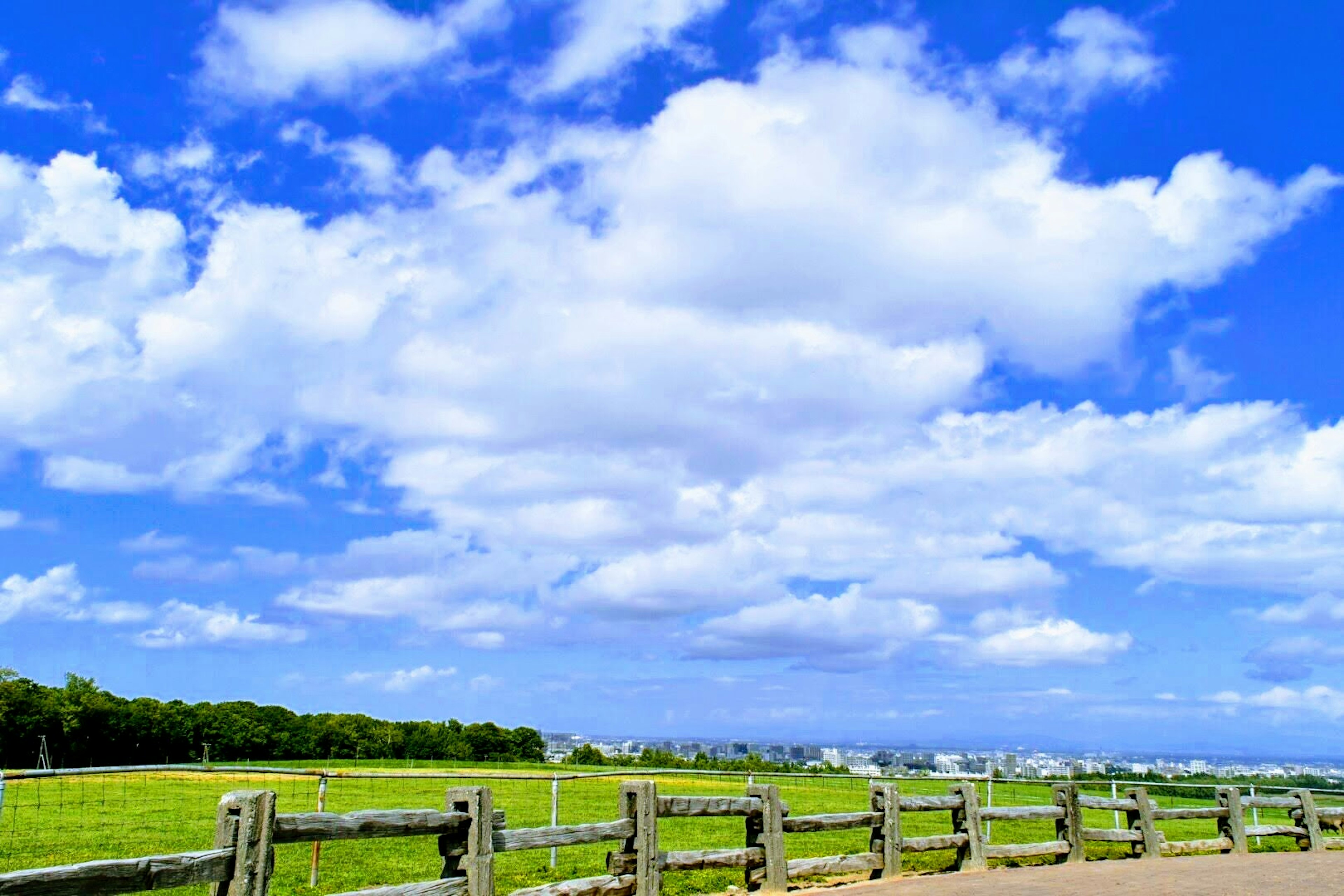 A landscape with blue sky and white clouds green meadow and wooden fence