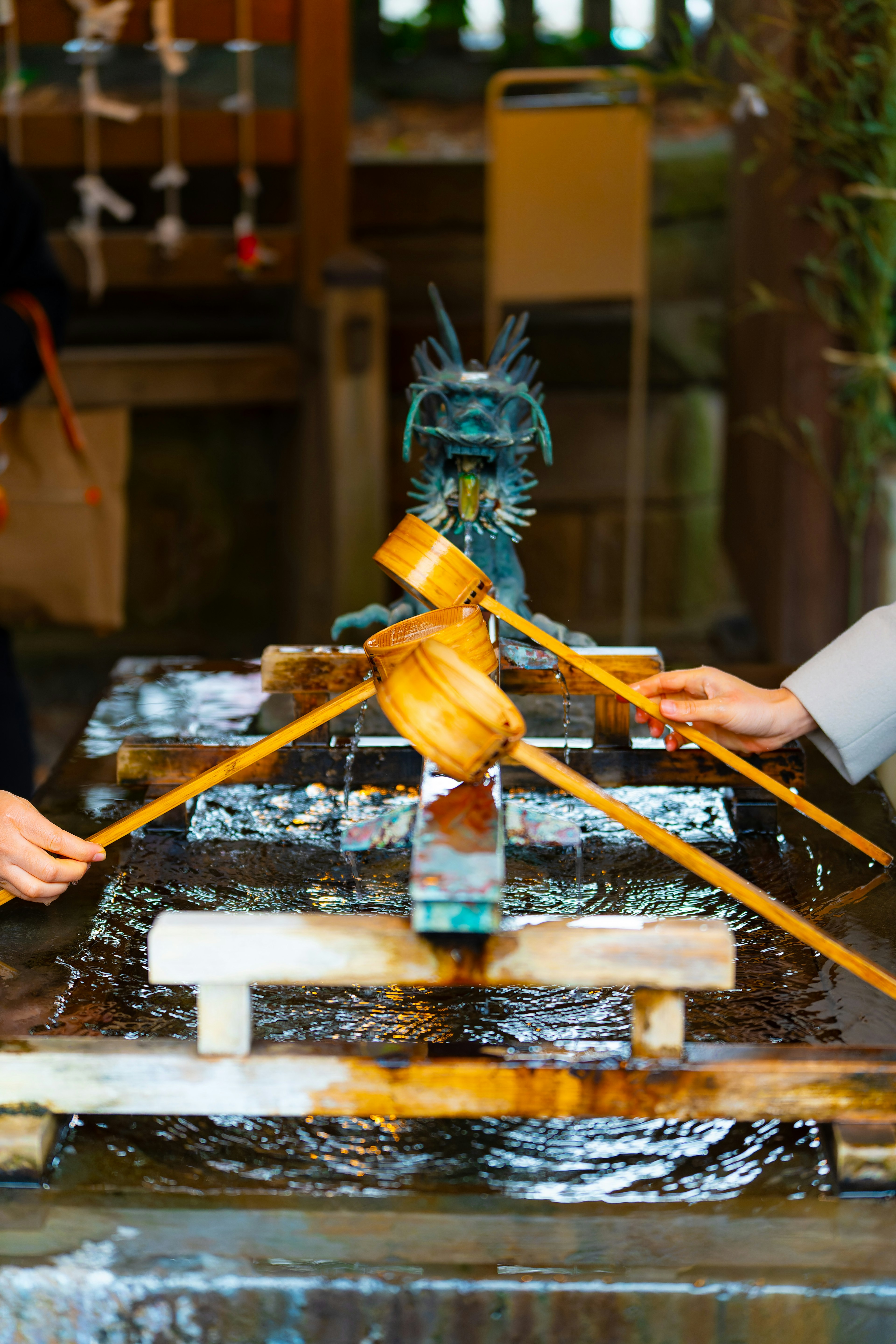 Deux mains utilisant des louches en bambou pour puiser de l'eau à une fontaine de purification shinto