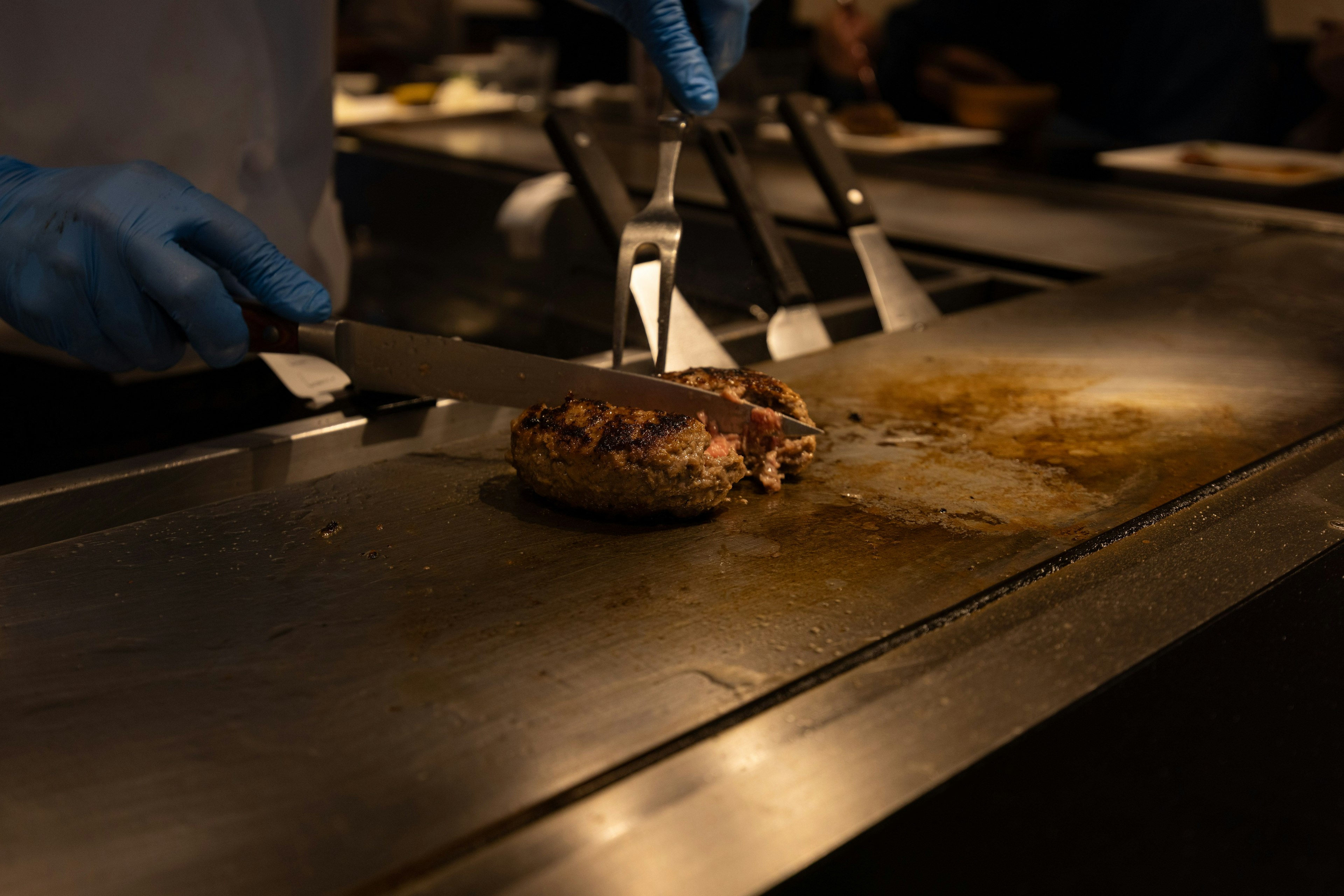 Koch mit blauen Handschuhen, der Fleisch auf einem Grill schneidet