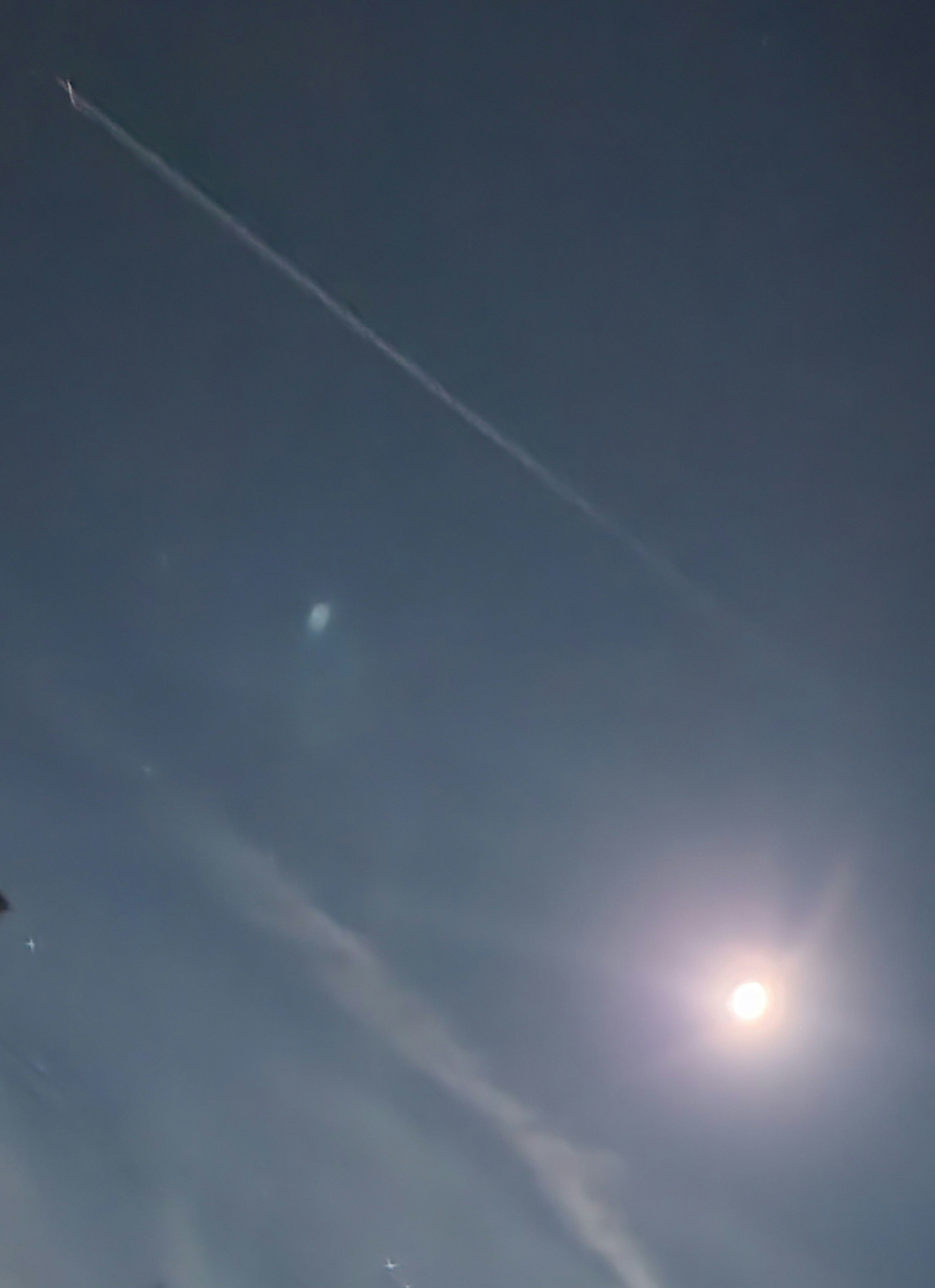 A clear sky with a contrail and a bright moon