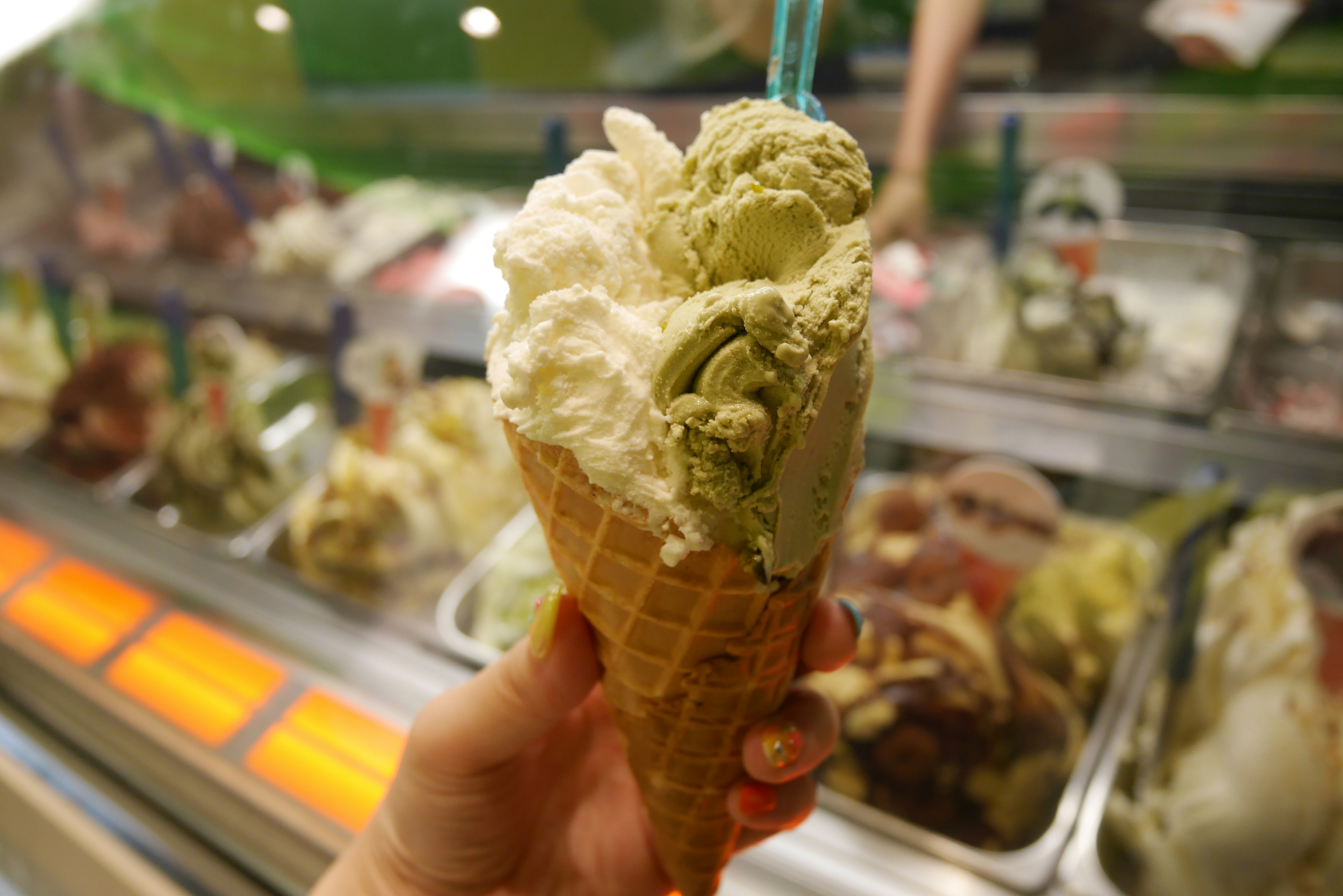 Photograph of a hand holding a cone filled with green and white ice cream