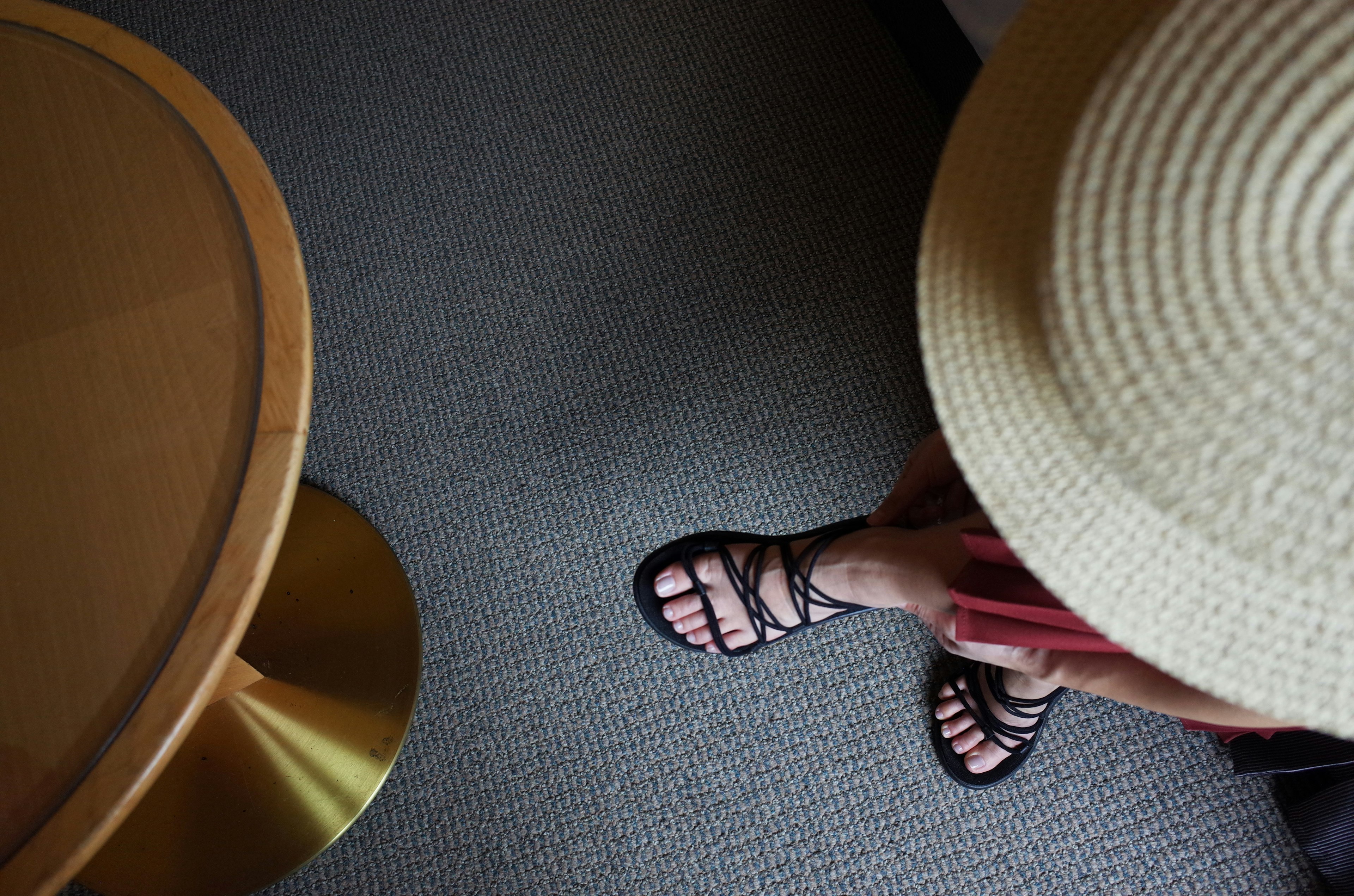 Photo of a person's feet wearing sandals with a straw hat and carpet in the background