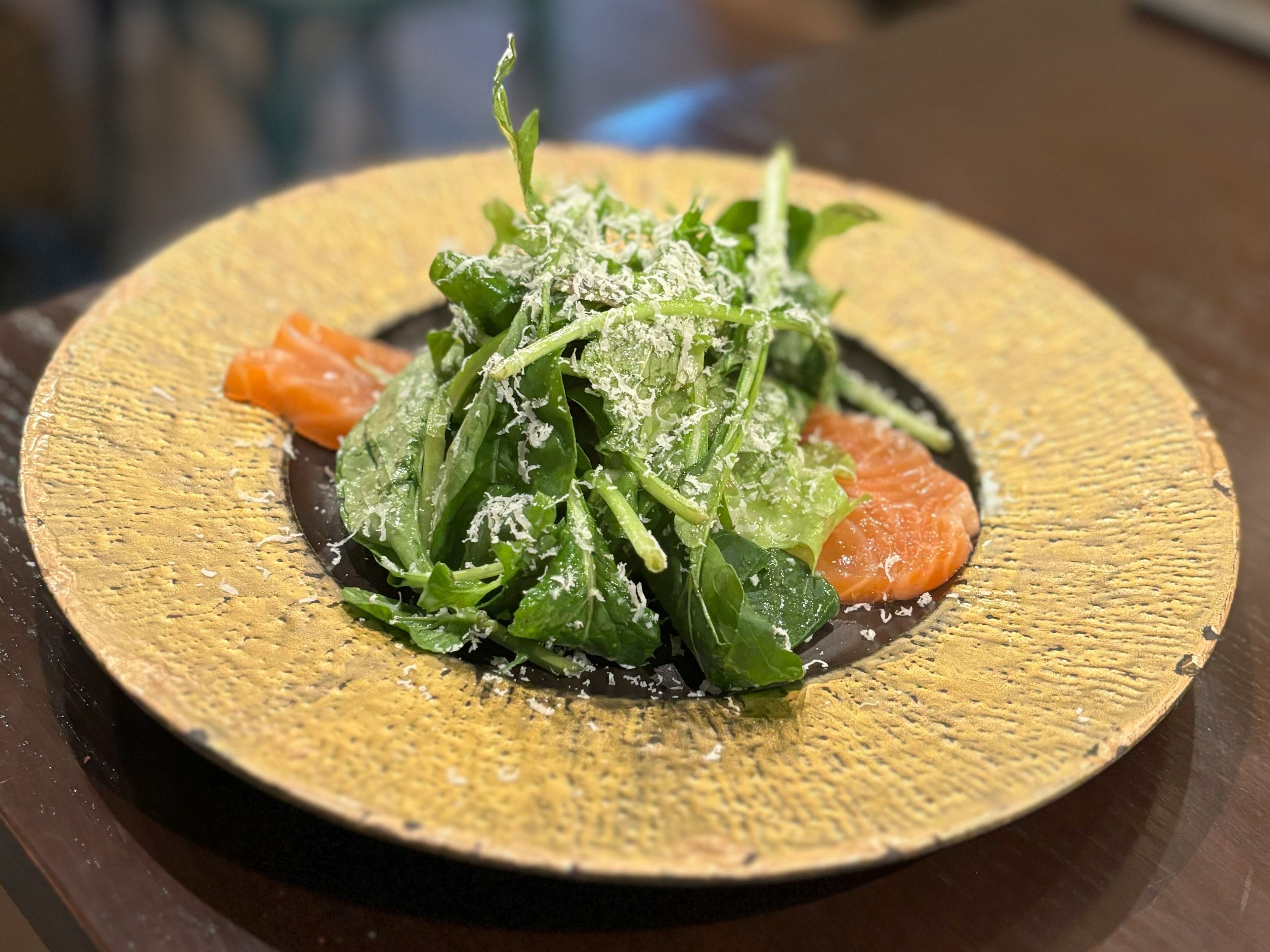 Salad served on a golden plate with slices of salmon and topped with parmesan cheese