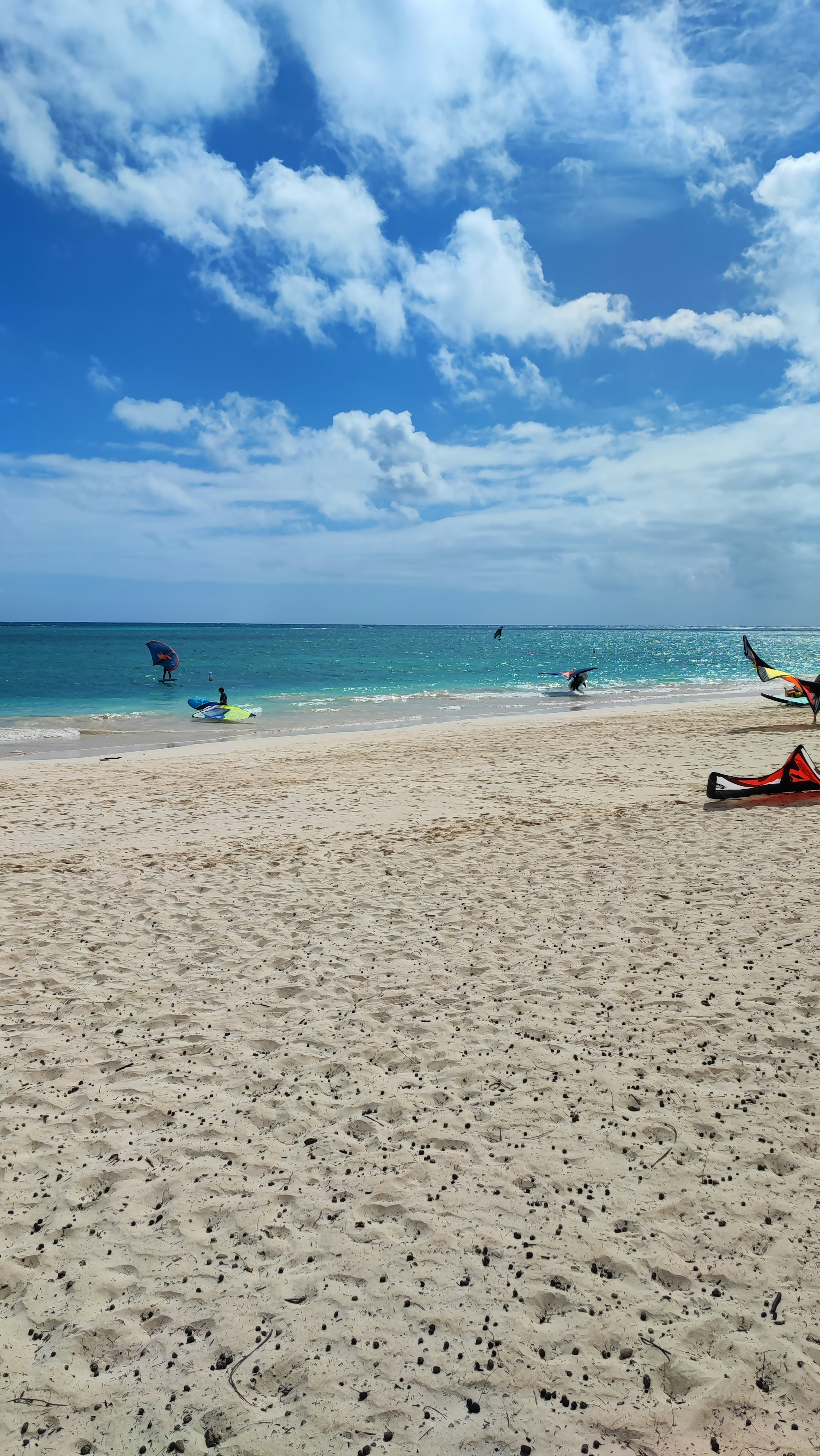 Una escena de playa con cielo azul y arena blanca donde la gente se divierte