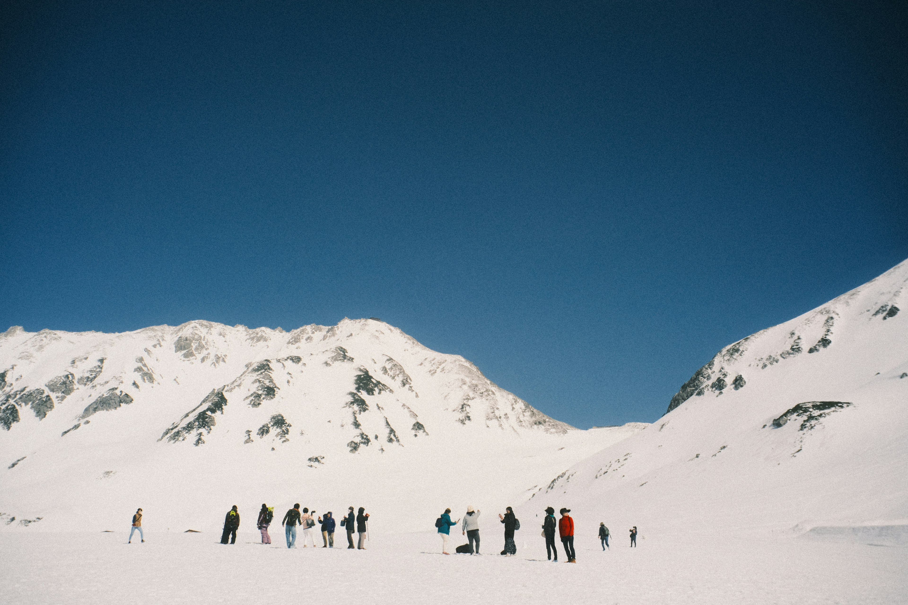 Groupe de personnes se tenant sur un paysage enneigé avec des montagnes et un ciel bleu clair