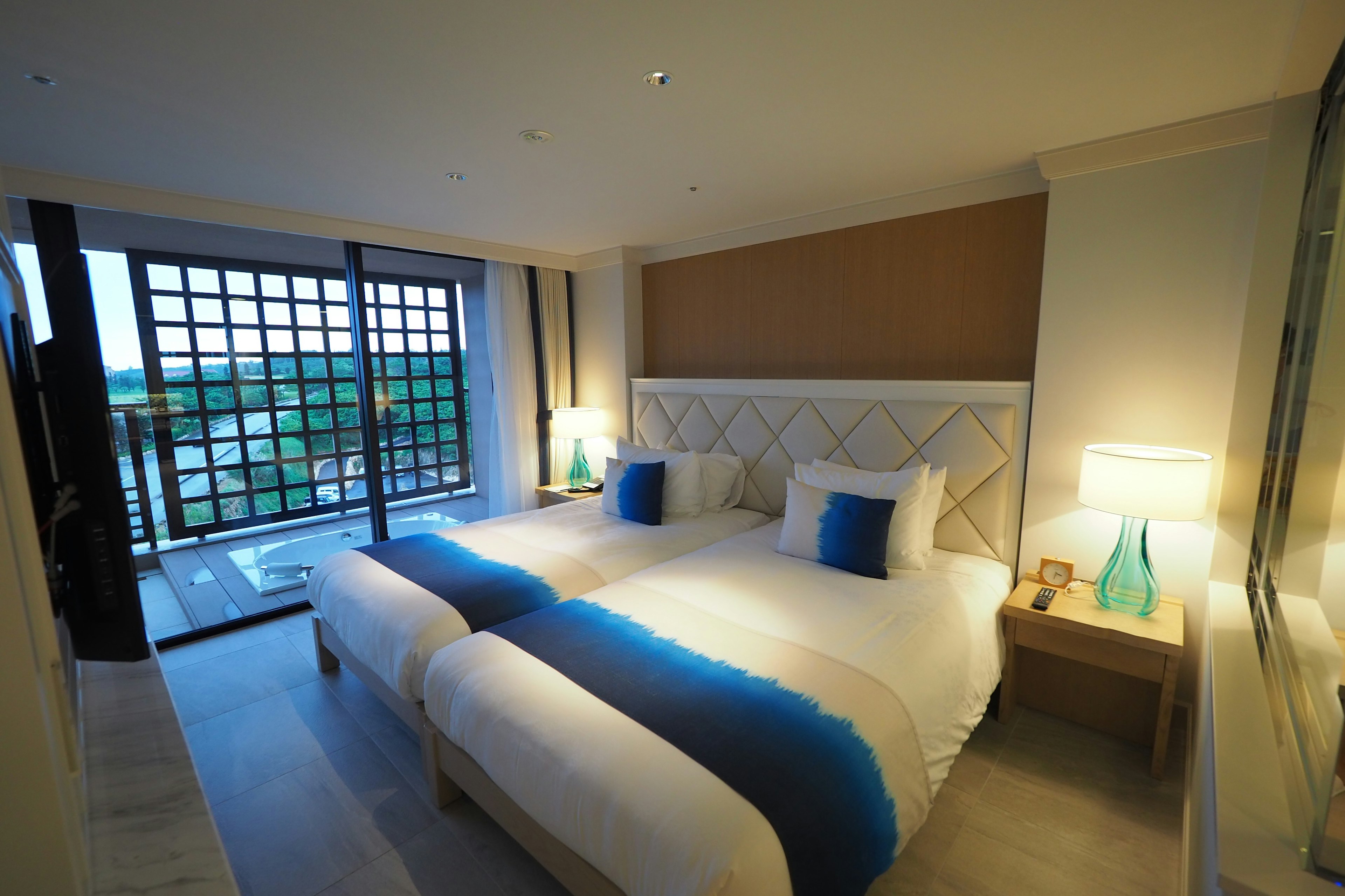 Kamar hotel modern dengan dua tempat tidur skema warna cerah dan jendela besar menunjukkan pemandangan luar