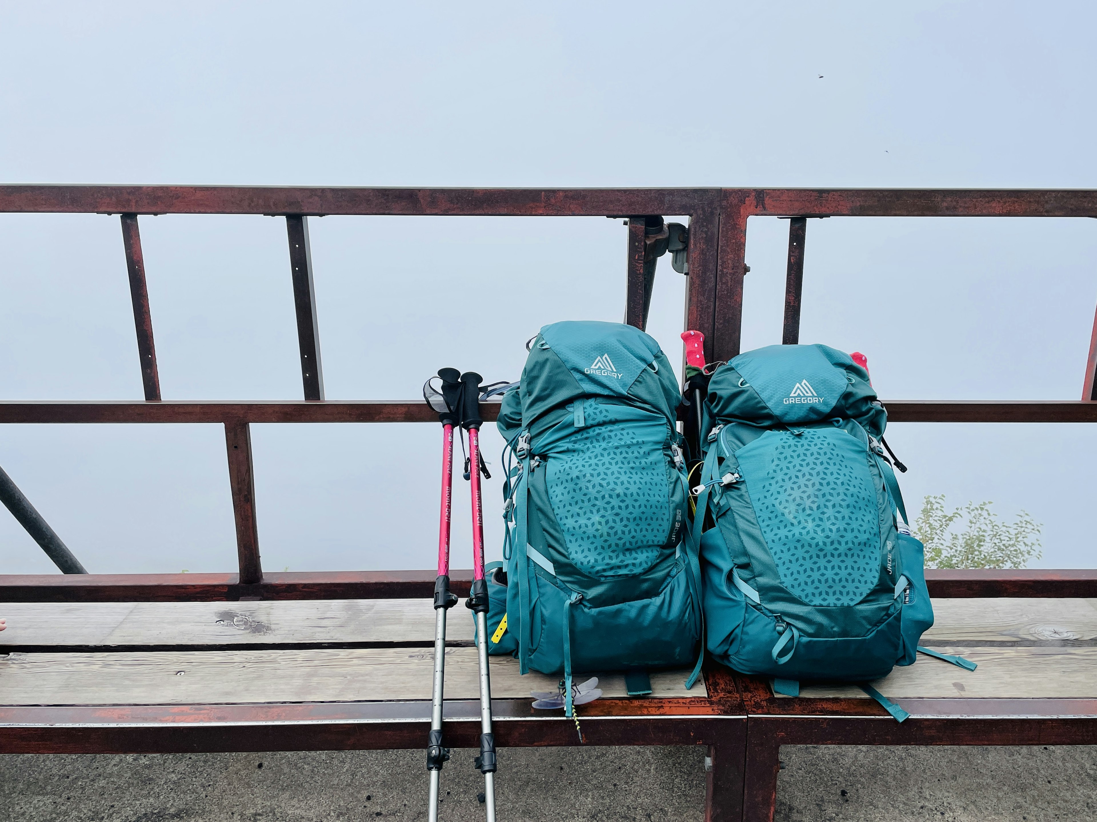 两个青色背包放在长椅上，旁边有登山杖