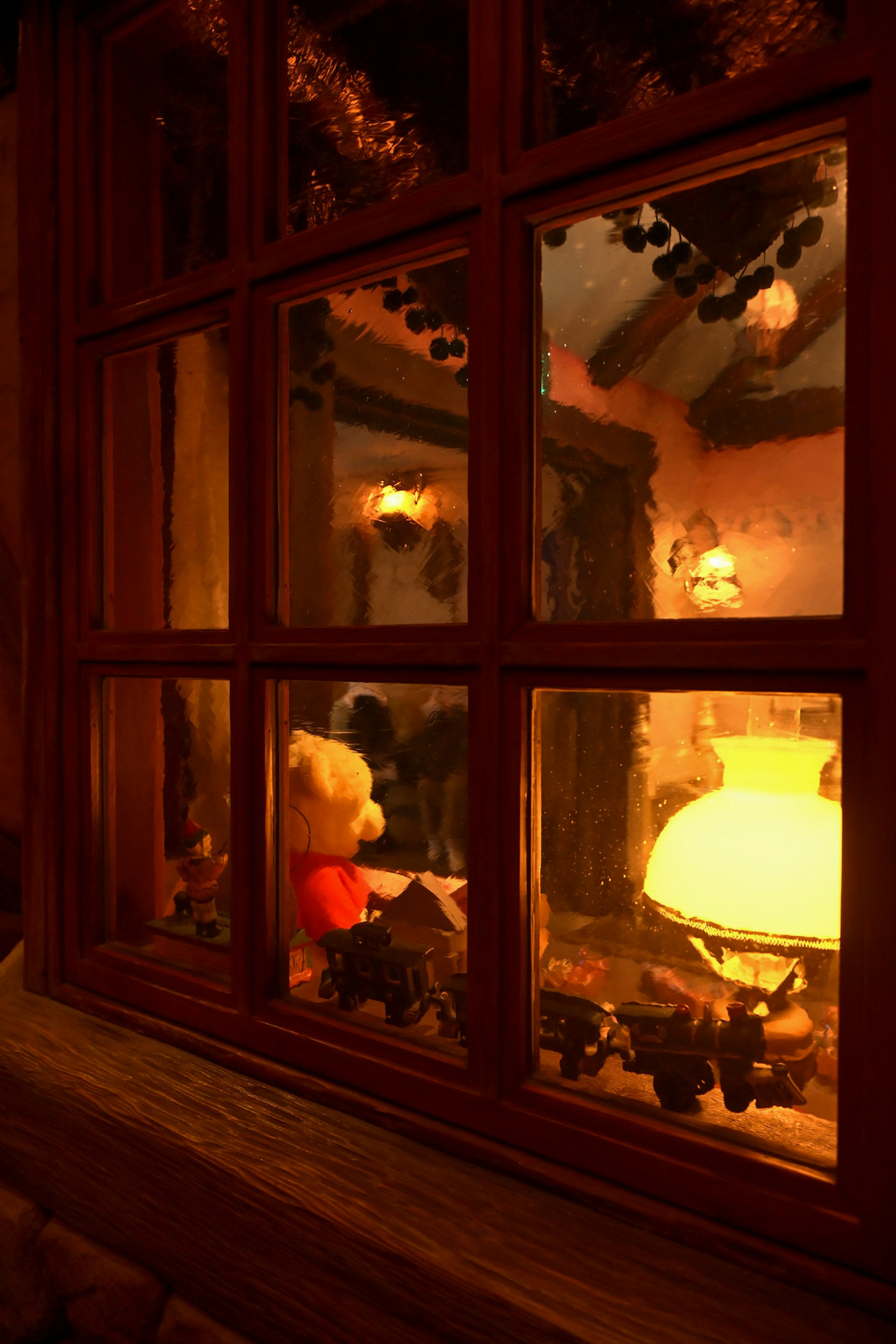 Warmly lit room seen through a window with a teddy bear and lamp