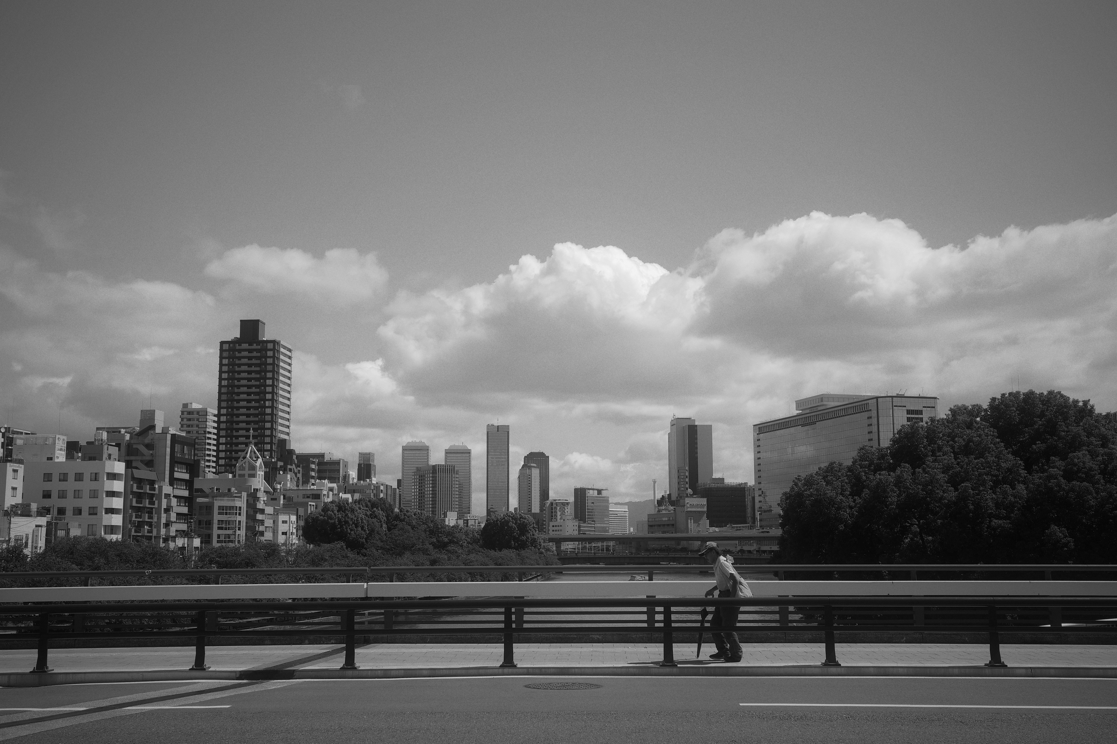 Paisaje urbano en blanco y negro con una persona caminando y nubes en el cielo