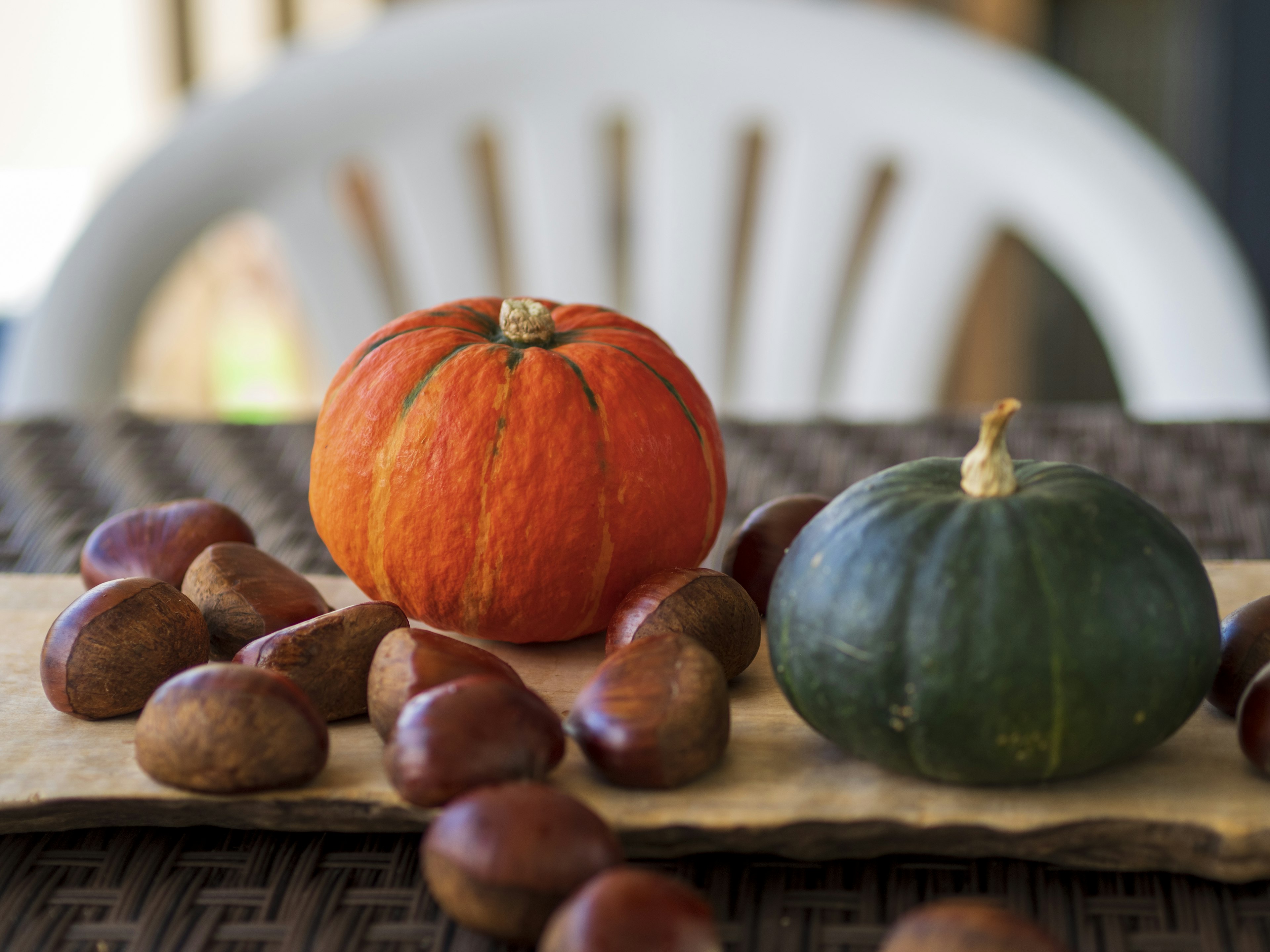 Orange pumpkin and green pumpkin on a table with chestnuts scattered around