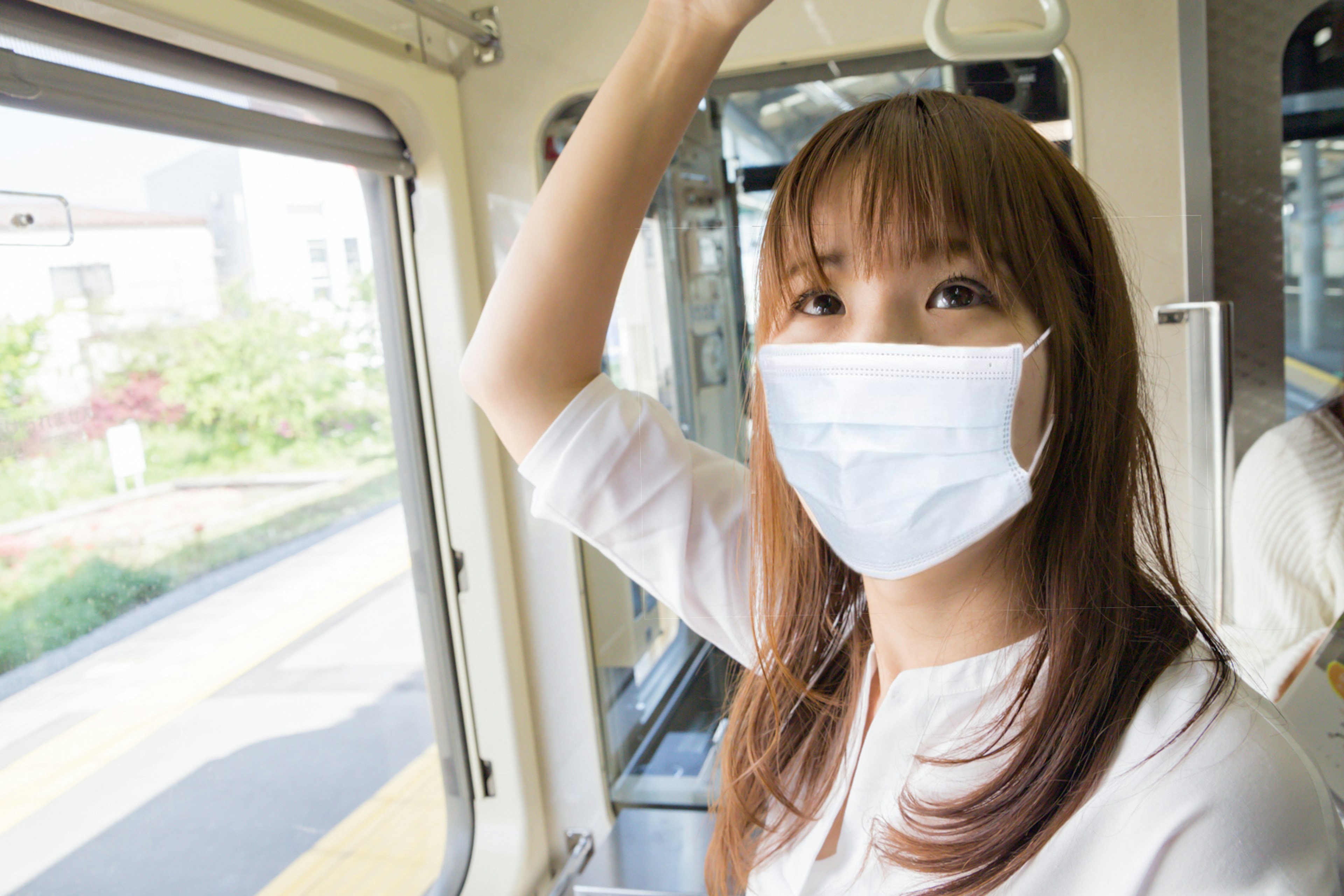 電車の中でマスクを着用した女性が手を上げている