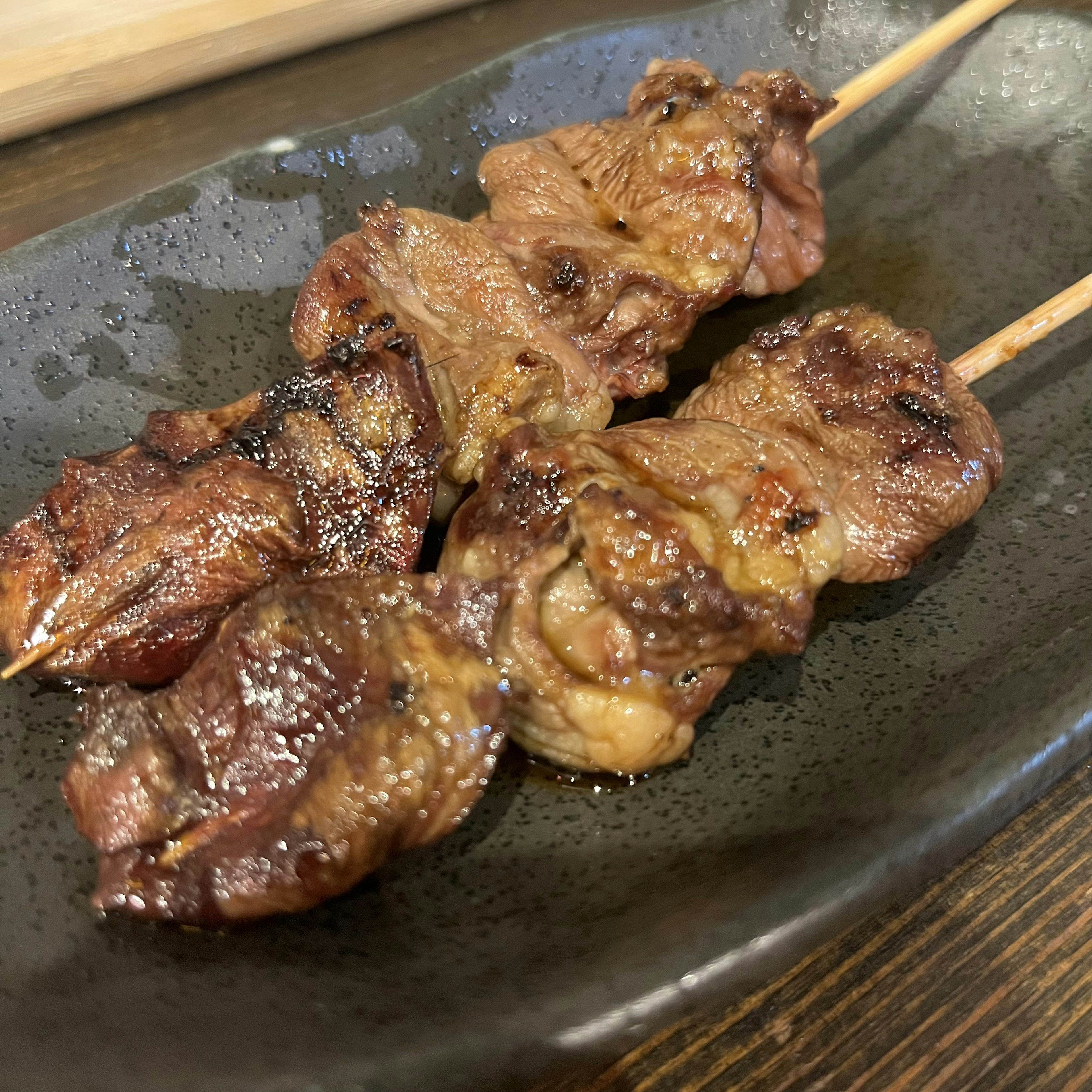 Sate yakitori panggang disajikan di atas piring hitam