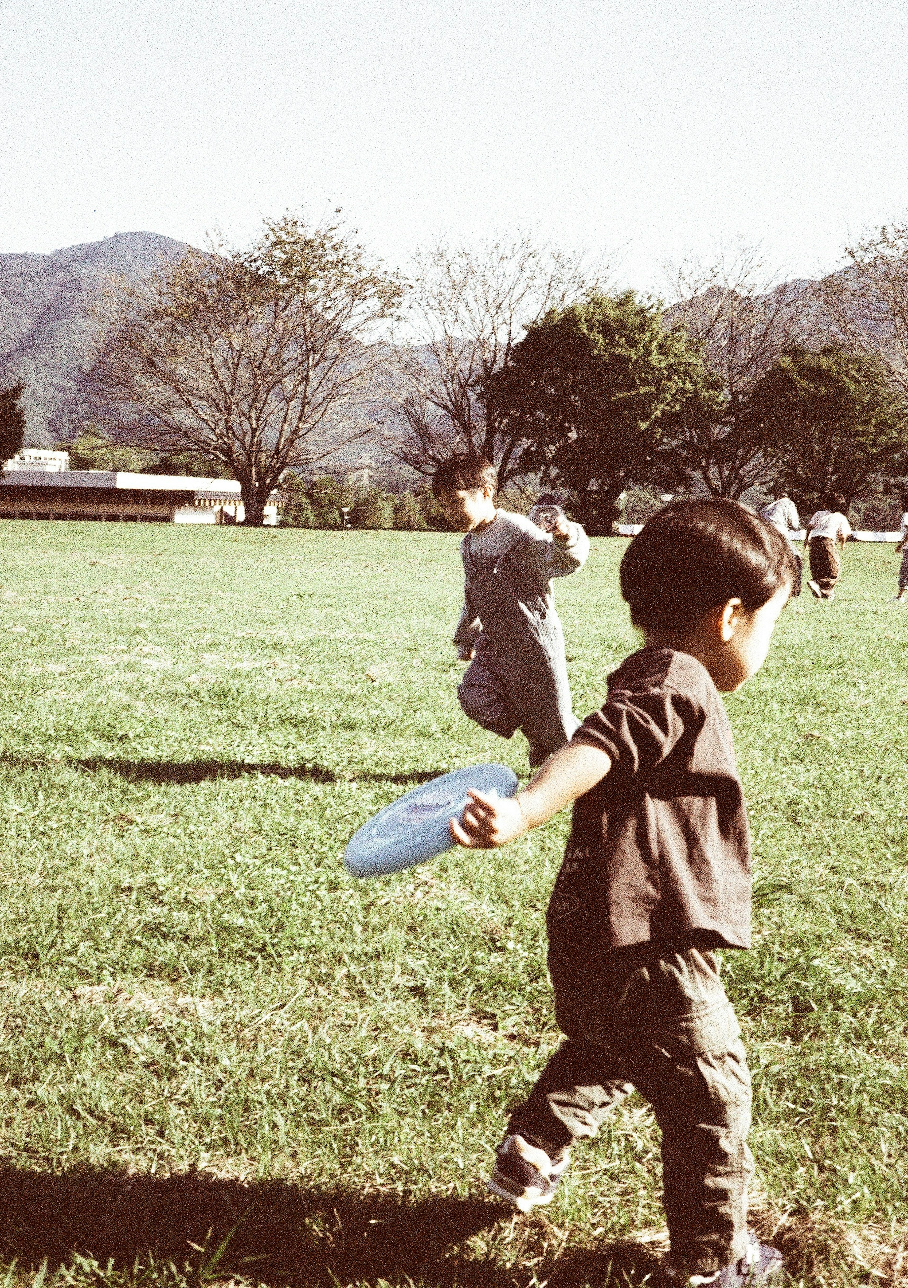 公園裡孩子們玩耍的照片 一個小男孩手裡拿著藍色飛盤 背景是山和樹木