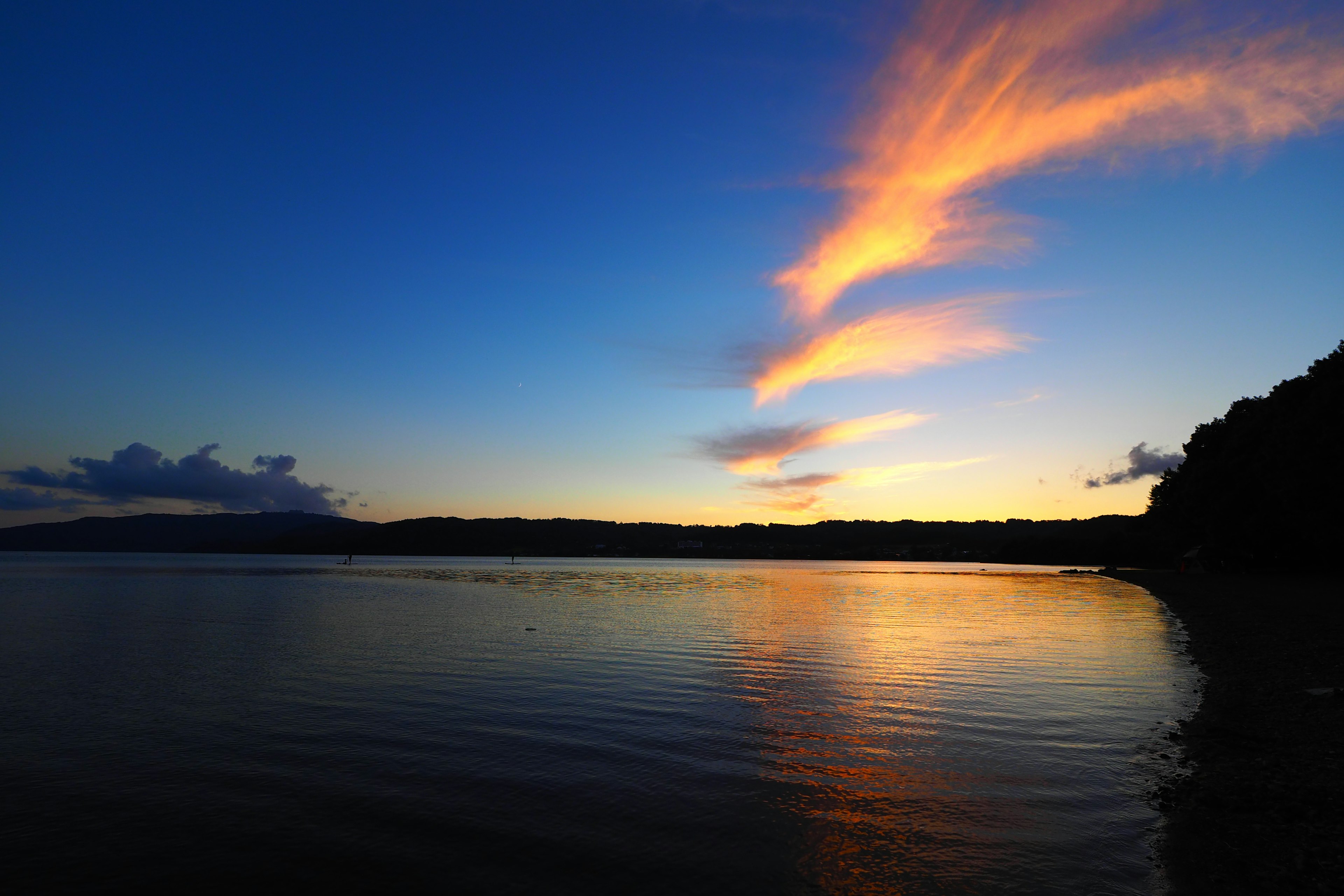 Ruhiger See bei Sonnenuntergang mit orangefarbenen Wolken und Reflexionen auf dem Wasser