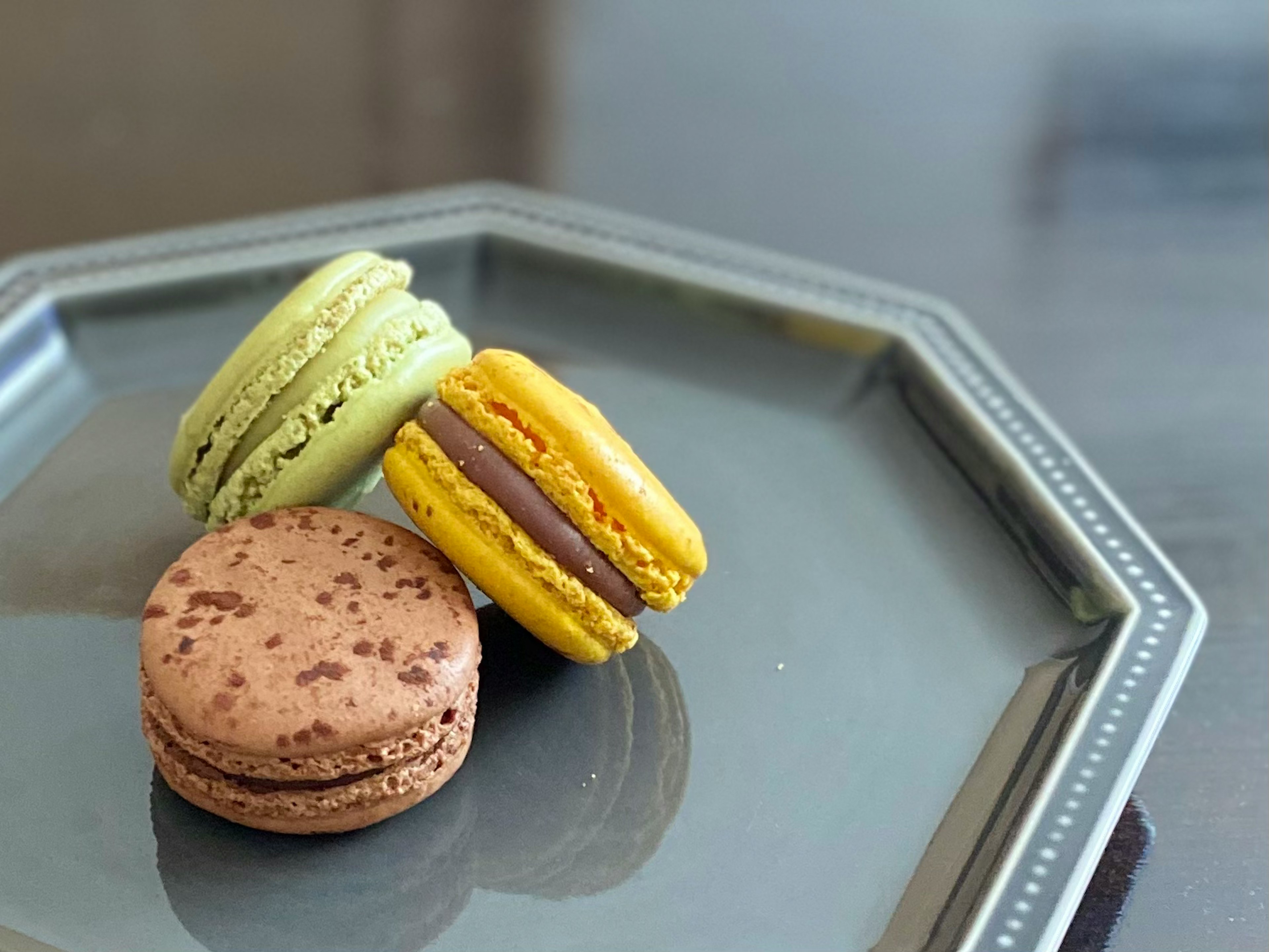 Trois macarons colorés sur une assiette argentée saveurs verte jaune et brune