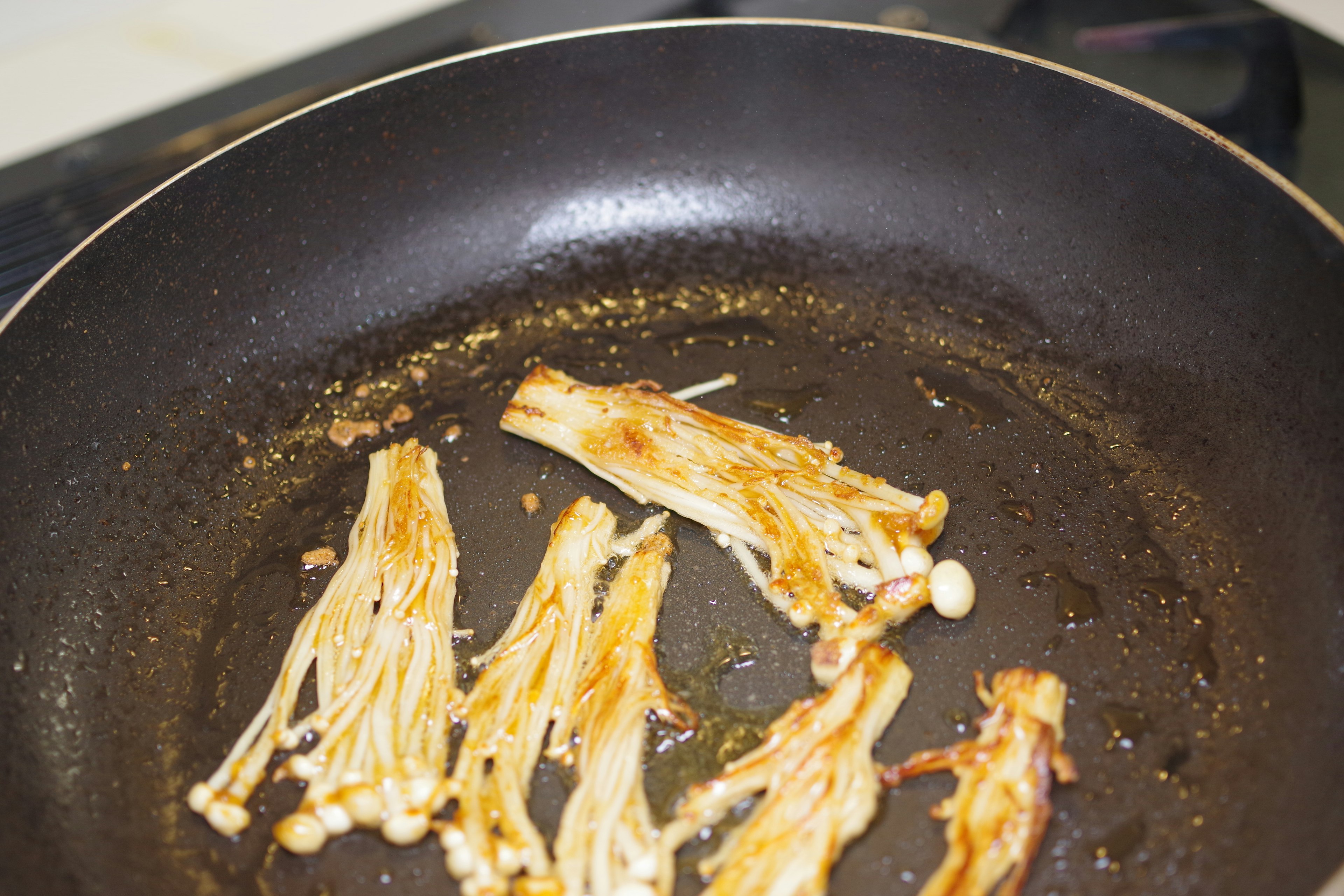 Sliced enoki mushrooms being cooked in a frying pan