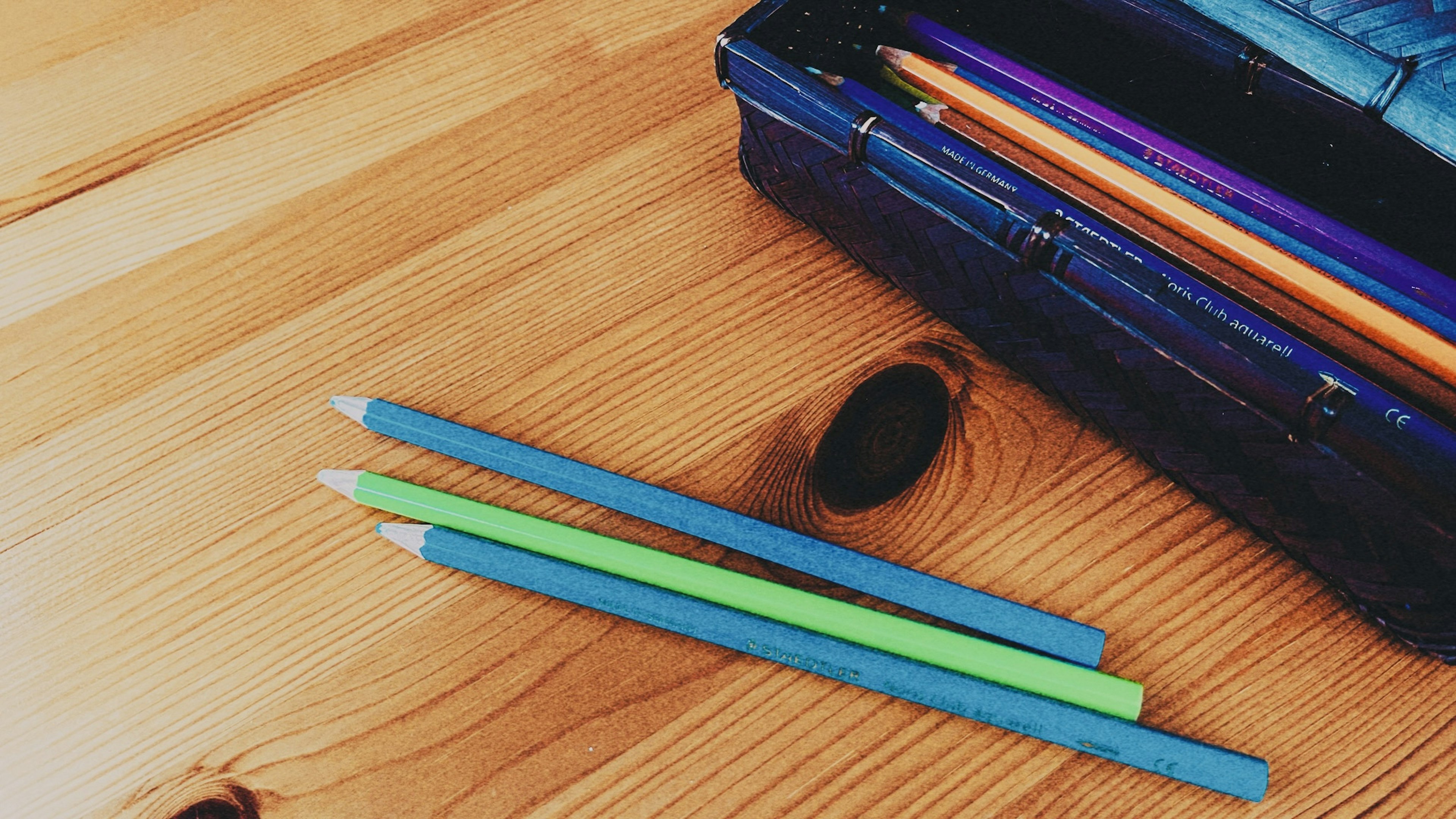 Gambar pensil warna biru dan hijau di atas meja kayu