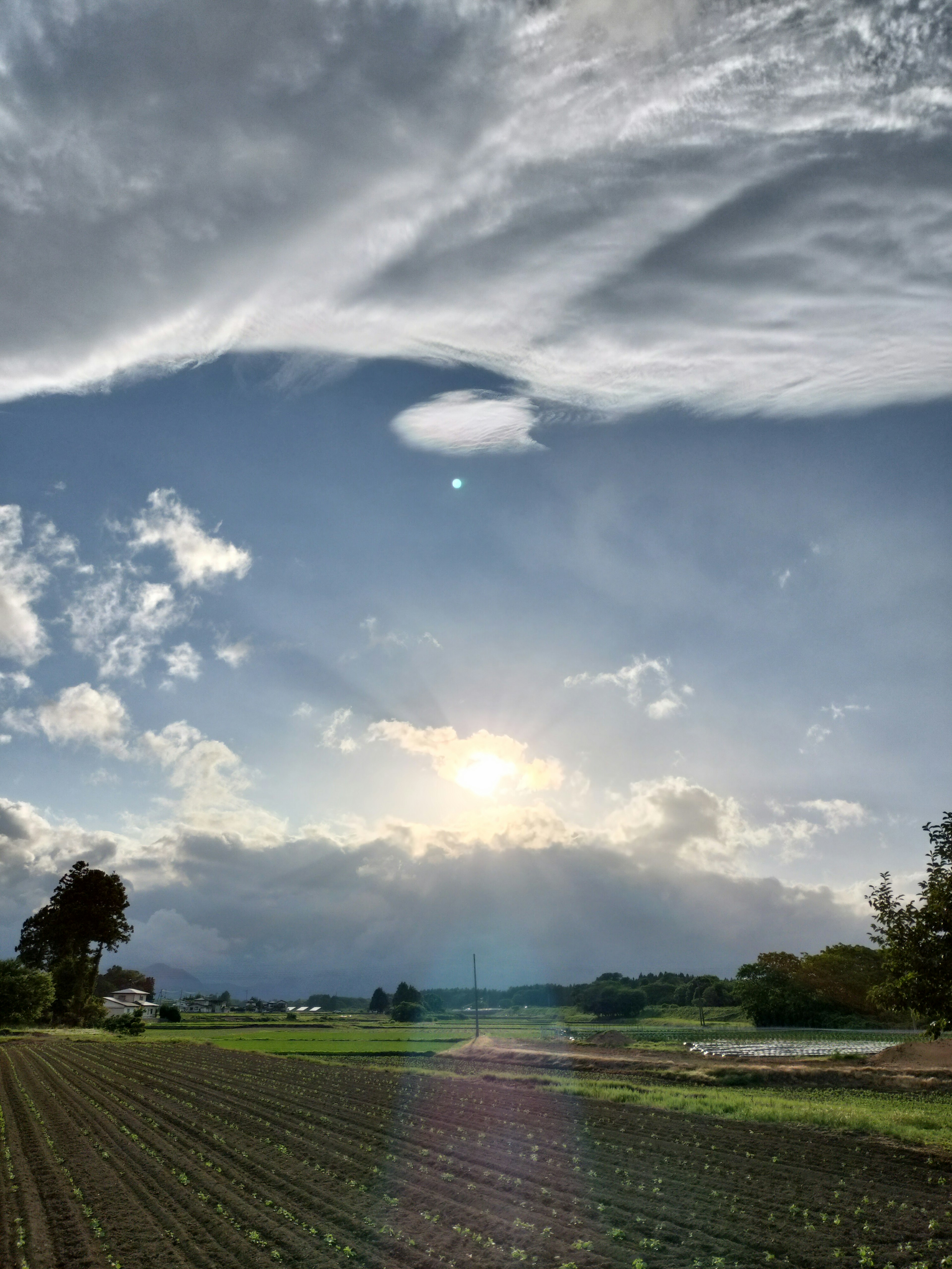 青空と雲に包まれた田園風景の夕日