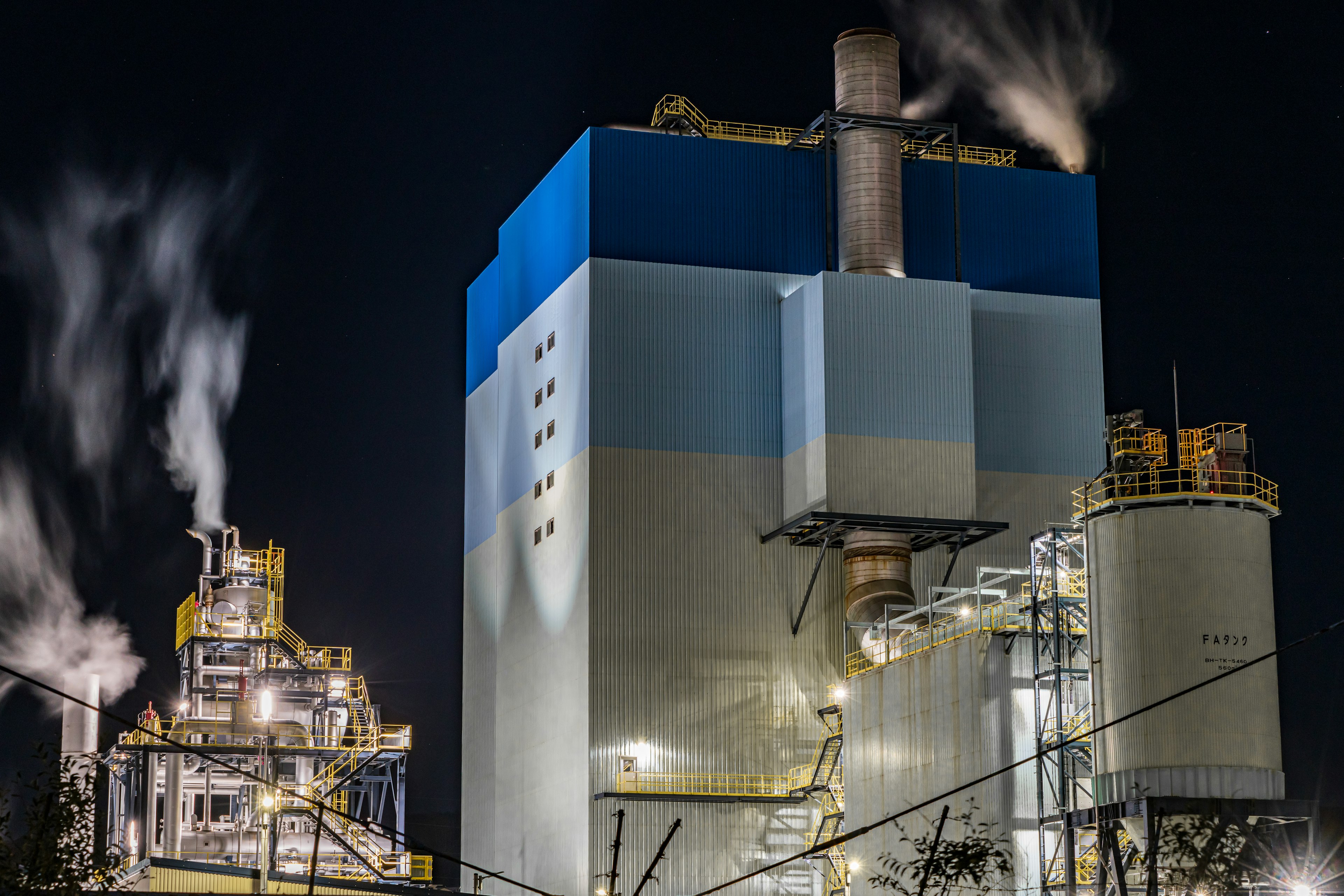 Nachtansicht einer Industrieanlage mit Rauch, der aus Schornsteinen aufsteigt