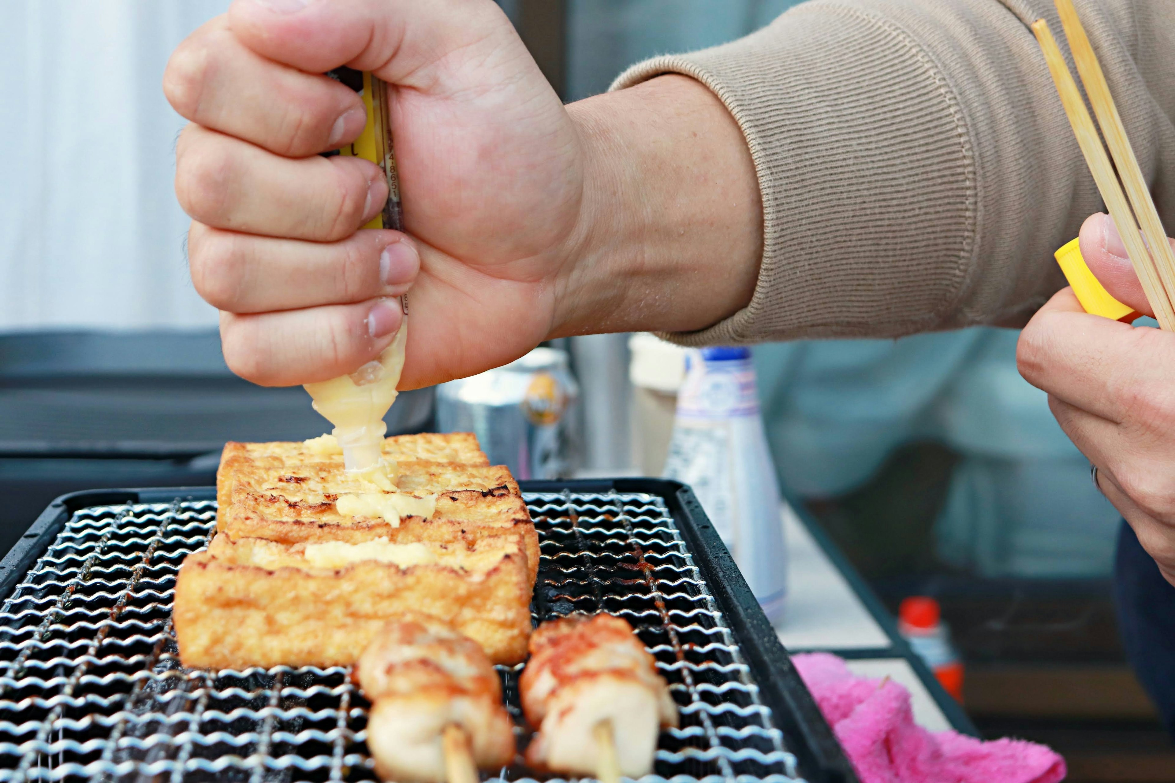 グリルで焼かれた豆腐の上にソースをかける手